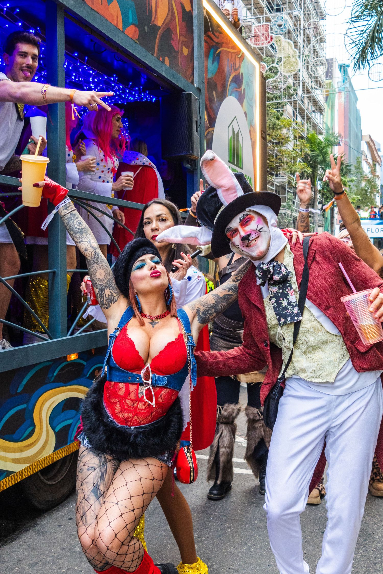 Costumed performers in theatrical makeup pose and celebrate during Mardi Gras festivities on a decorated street.