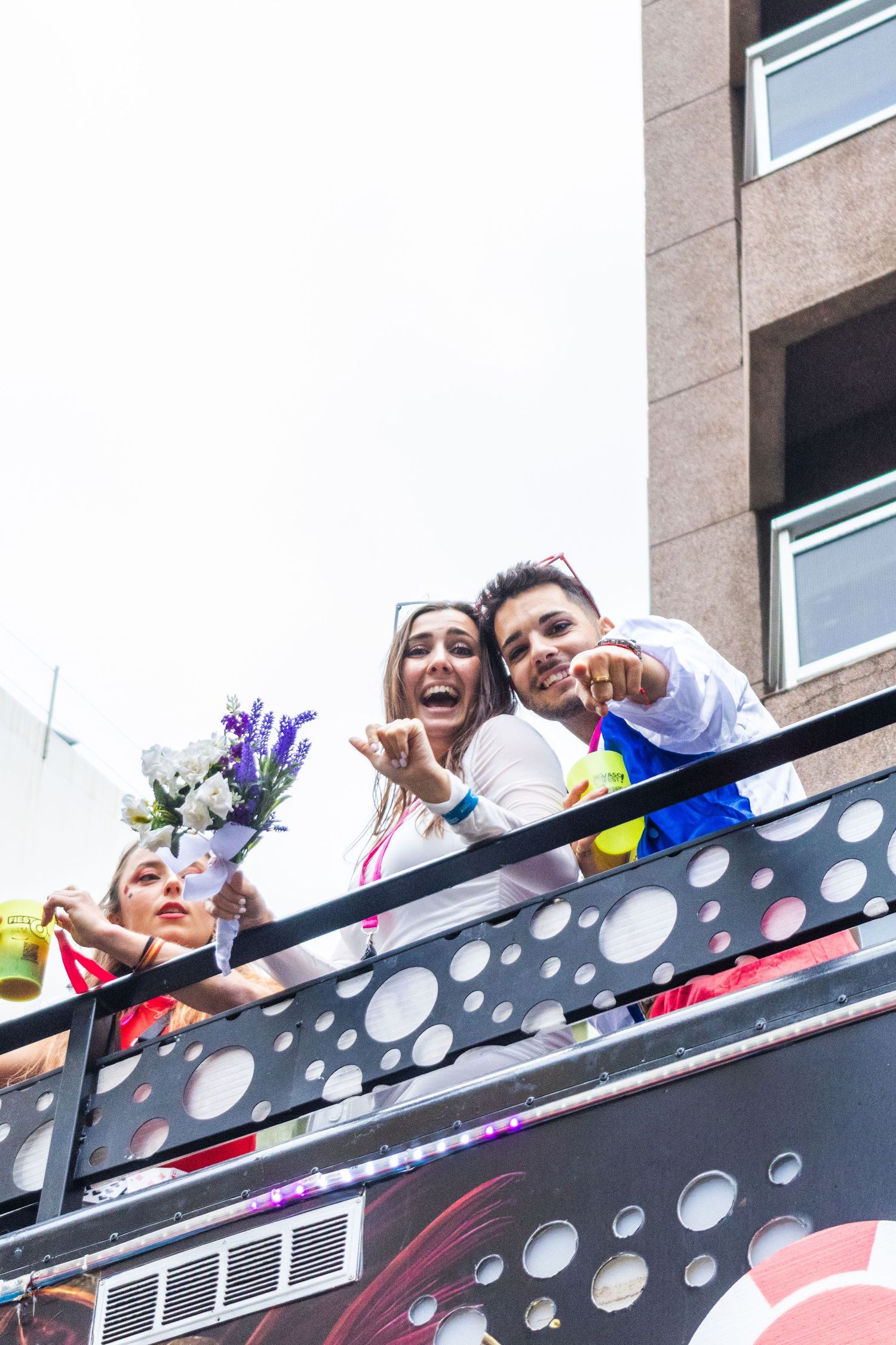 A group of people lean over a polka-dotted balcony railing while laughing and smiling together.