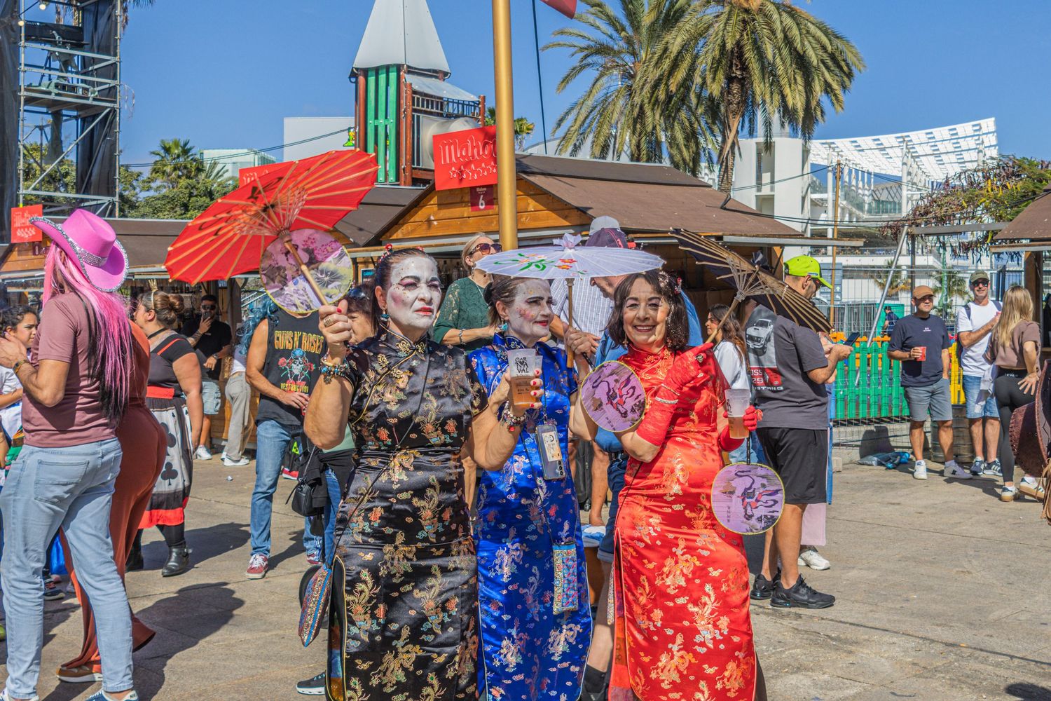 Colorful parasols and traditional Chinese dresses add festive atmosphere to an outdoor market or festival on a sunny day.