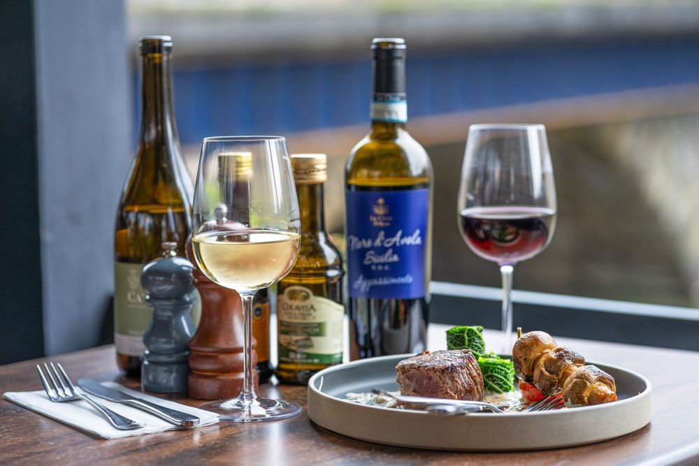 Wine glasses and bottles arranged on a rustic wooden table in a restaurant setting with ambient lighting.