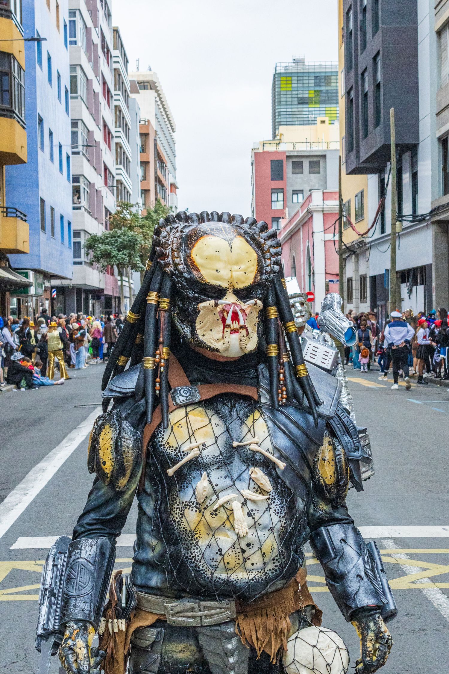 Detailed Predator costume cosplay with intricate armor on display at a crowded street festival.