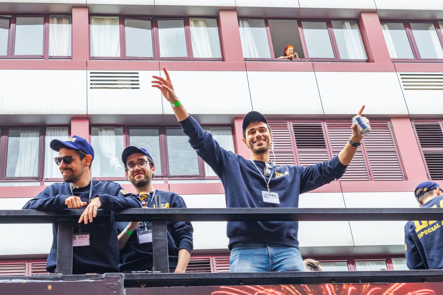 Enthusiastic fans celebrate from a balcony during a sports event, raising their arms in excitement.