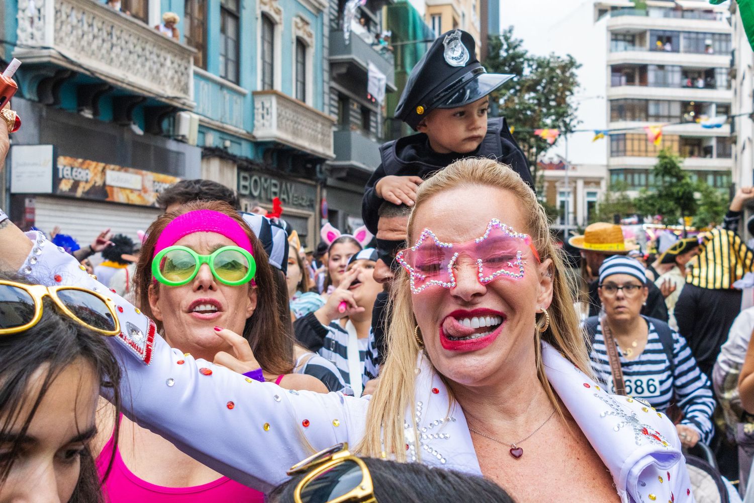 Festive crowd wearing colorful sunglasses and bright outfits celebrates at an outdoor summer event.