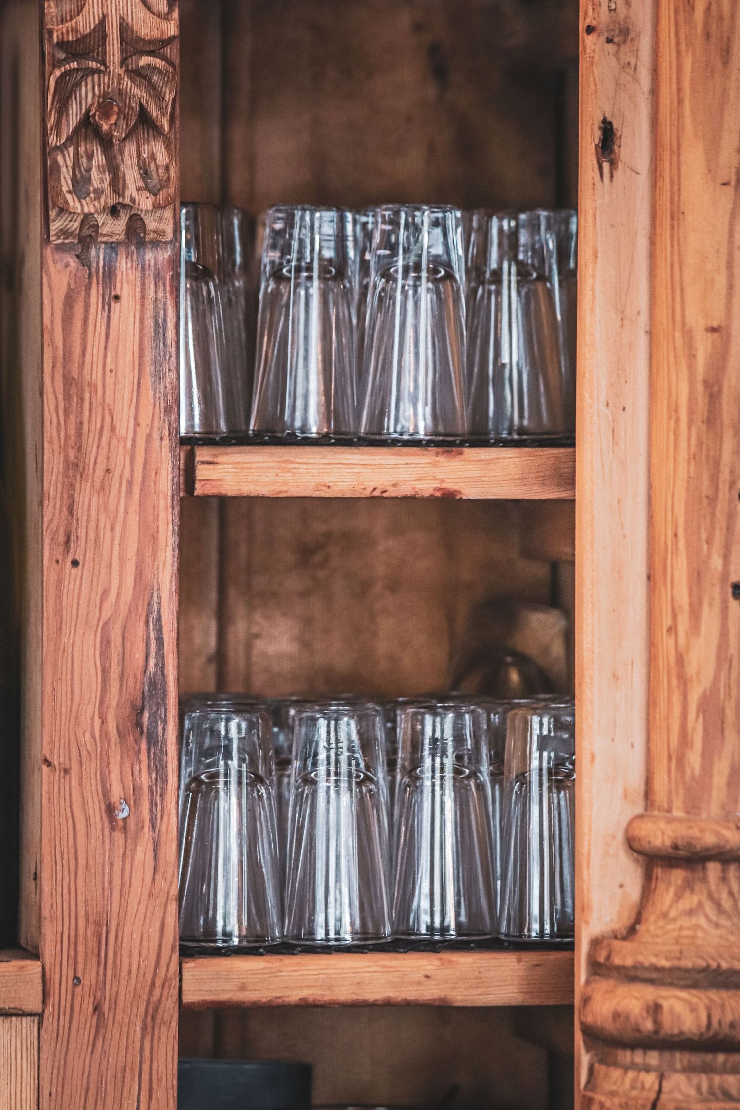 Glass bottles arranged neatly on rustic wooden shelves in a vintage cabinet display.