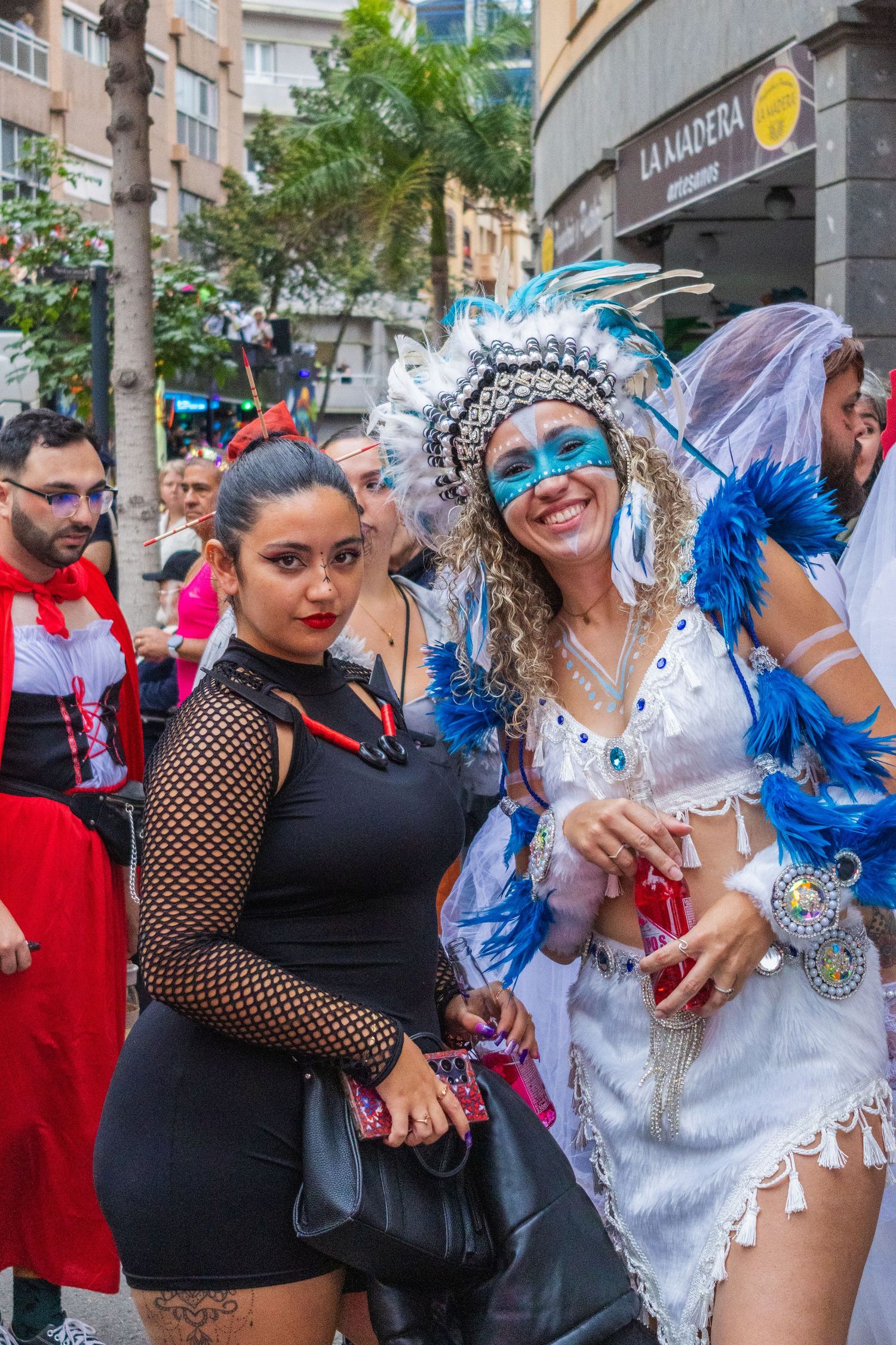 Carnival dancers in blue and white costumes perform at a street festival with onlookers watching the celebration.