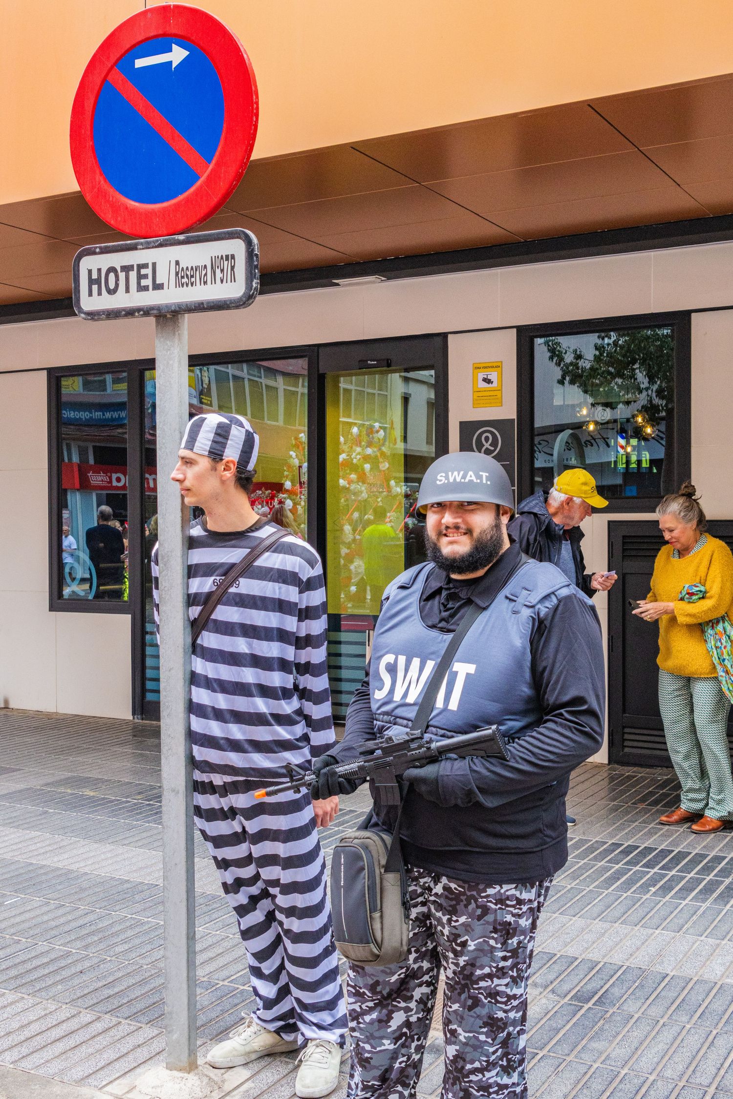 People in costumes interact on a sidewalk outside a building with a hotel sign and no parking symbol.