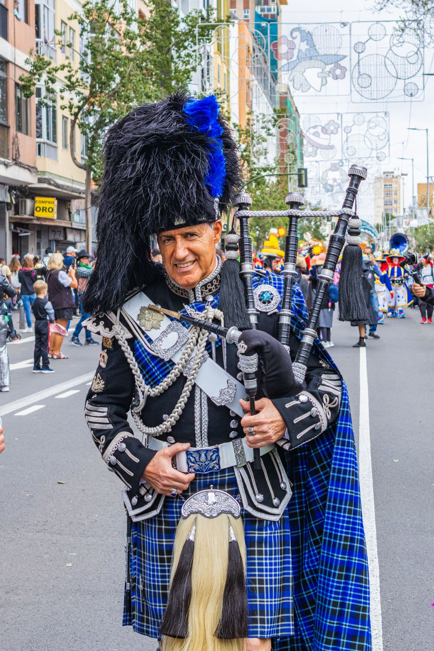 People in traditional Scottish kilts and military regalia perform during a parade celebration on a city street.