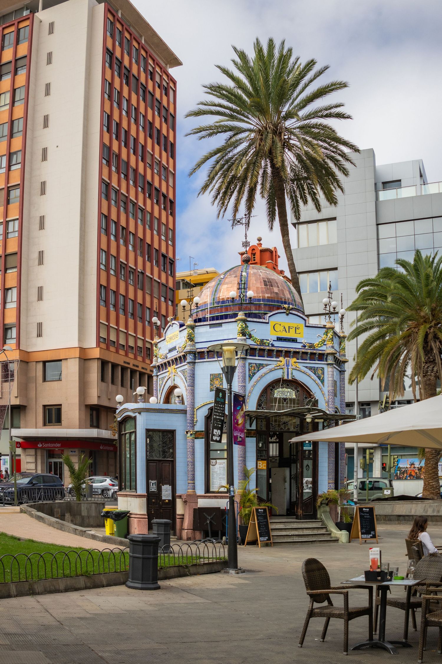 Ornate blue cafe building with dome roof beside palm trees and modern buildings in Las Palmas, Gran Canaria.