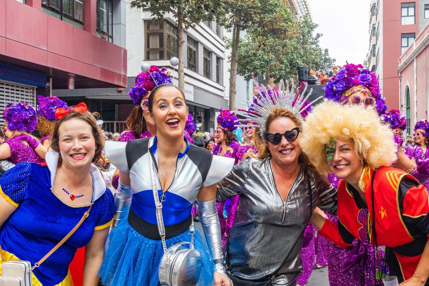 A group of people in colorful costumes and wigs celebrating at a pride parade or festival on a city street.