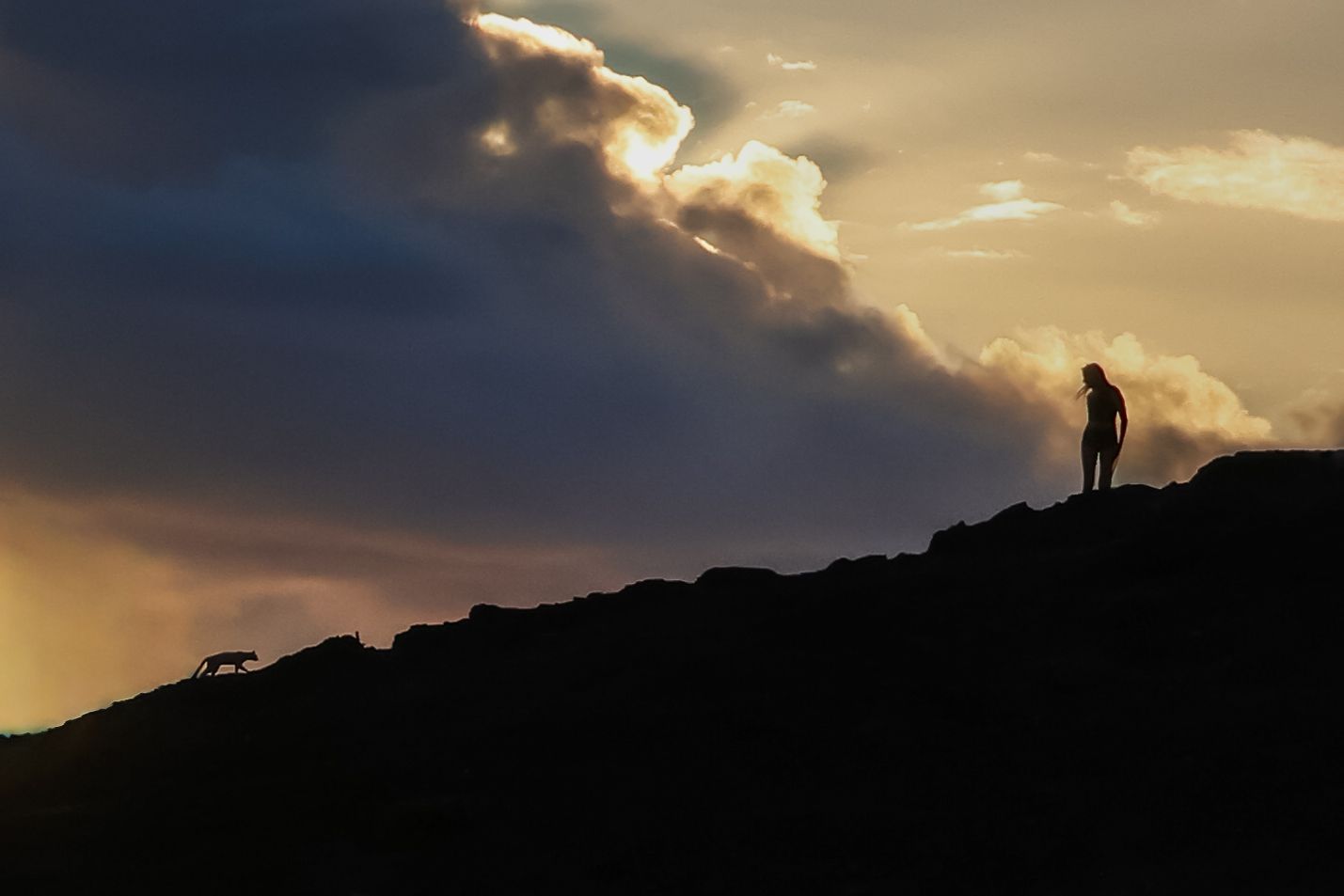 Dramatic sunset silhouette against cloudy sky over mountainous terrain.