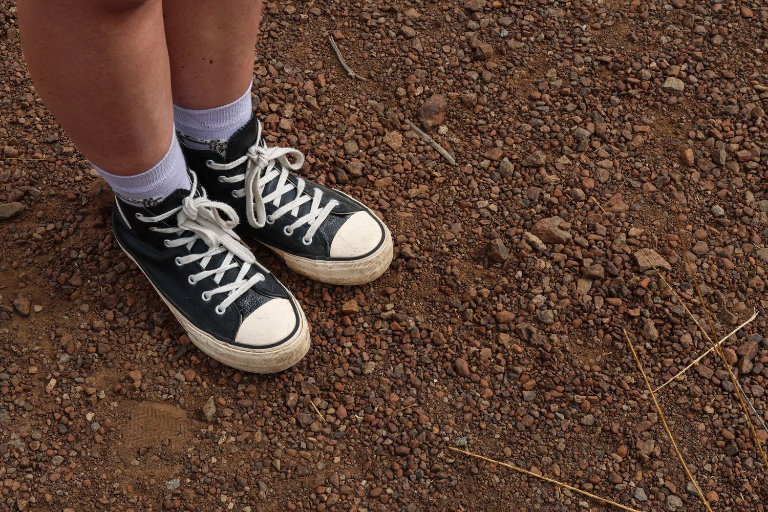 Classic black and white Converse sneakers with white socks on dirt ground.