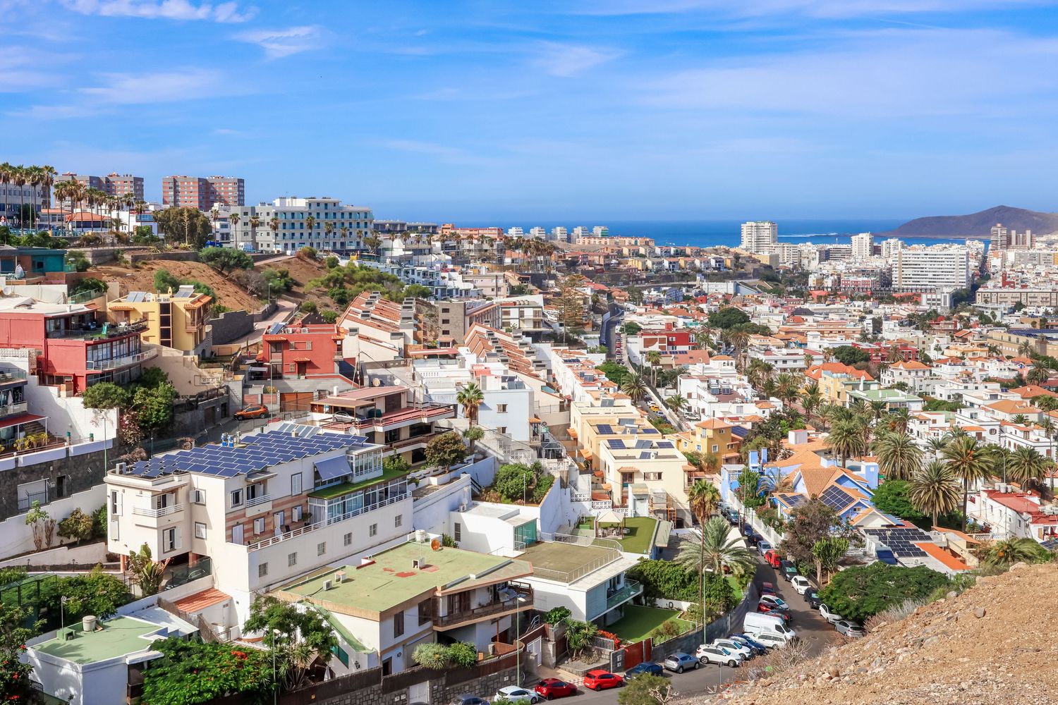 Aerial view of coastal city with colorful buildings cascading down hillside towards ocean.
