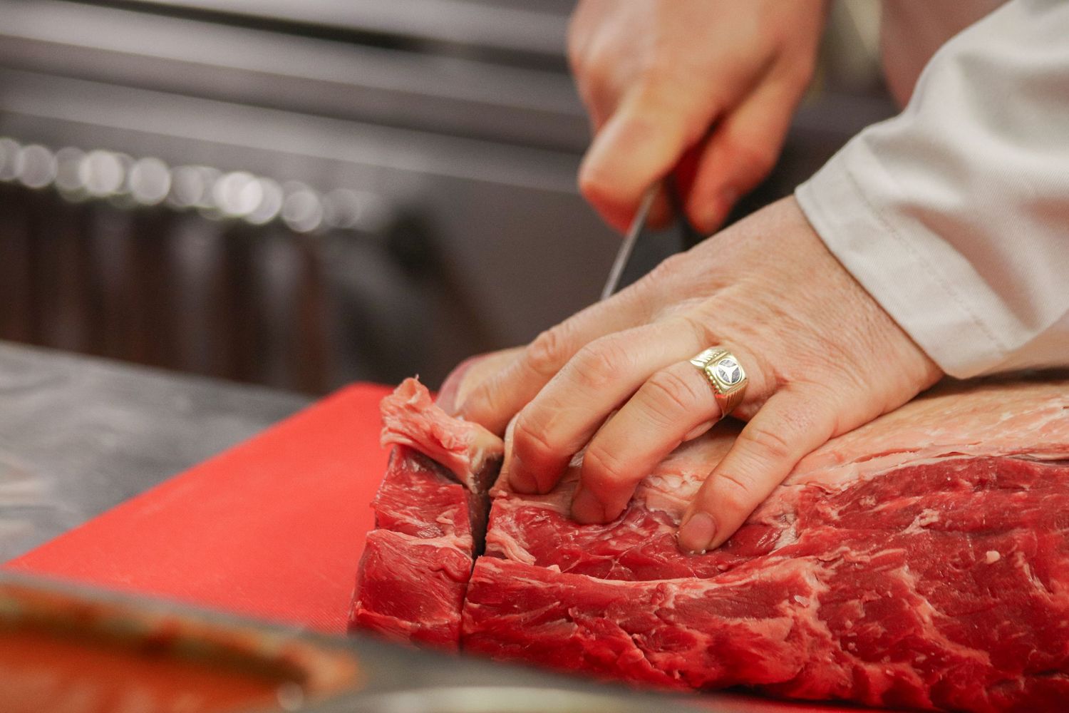 Close-up view of hands using a sharp knife to precisely cut and trim raw red meat on a cutting board.