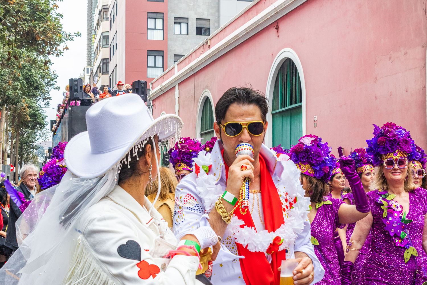Colorful Mardi Gras parade celebration with performers in elaborate purple and white costumes on city street.