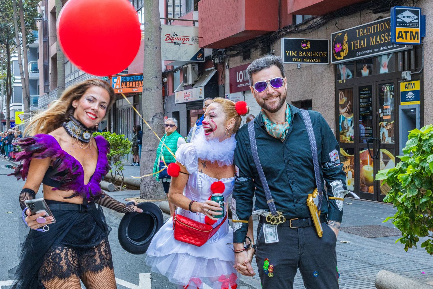 Costumed partygoers in steampunk and Victorian-inspired outfits pose on a city street with a red balloon.