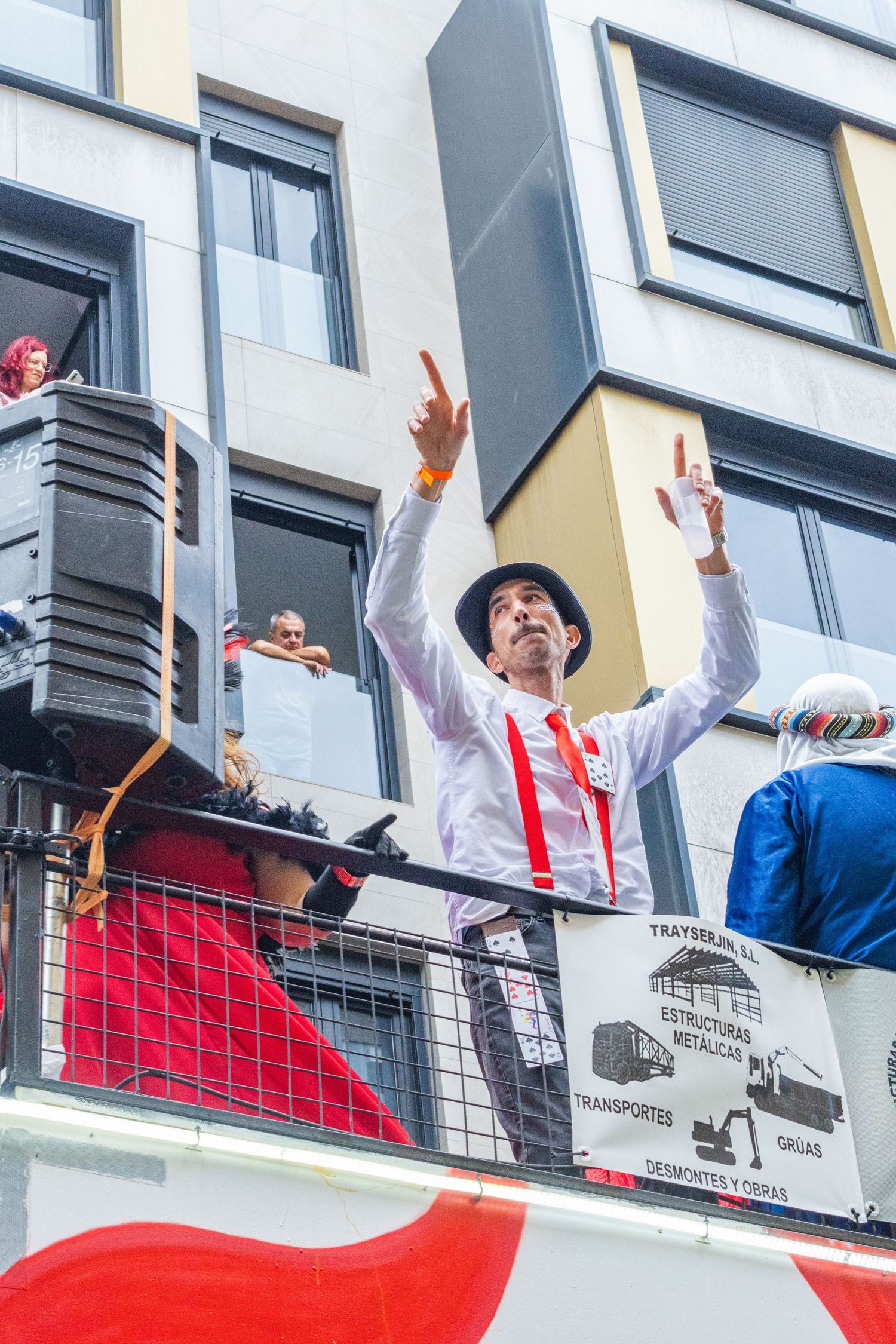 Soccer fans celebrate from a balcony wearing red and white jerseys with arms raised in excitement.