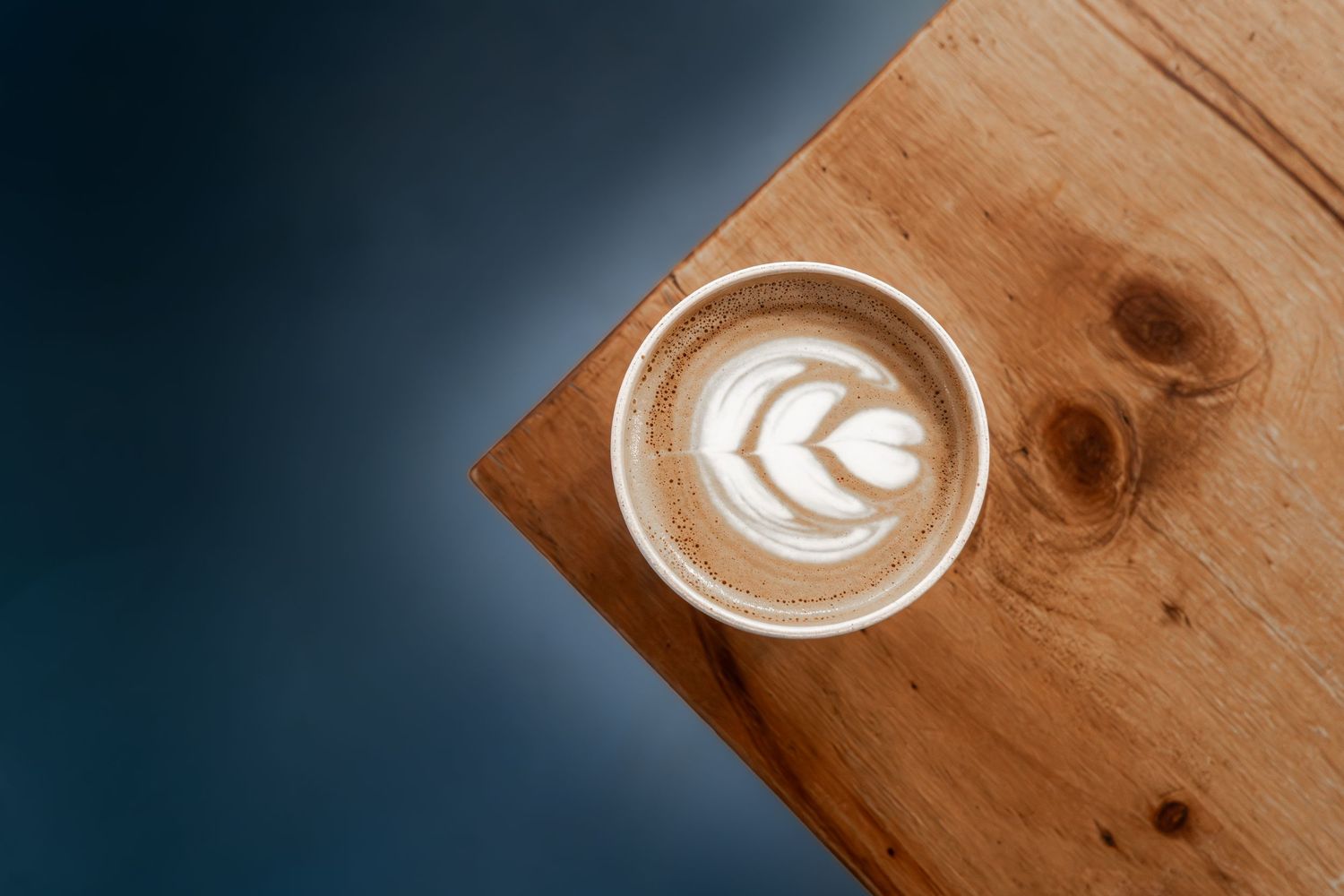 Overhead view of a latte art coffee in a white cup on a rustic wooden board against a dark background.