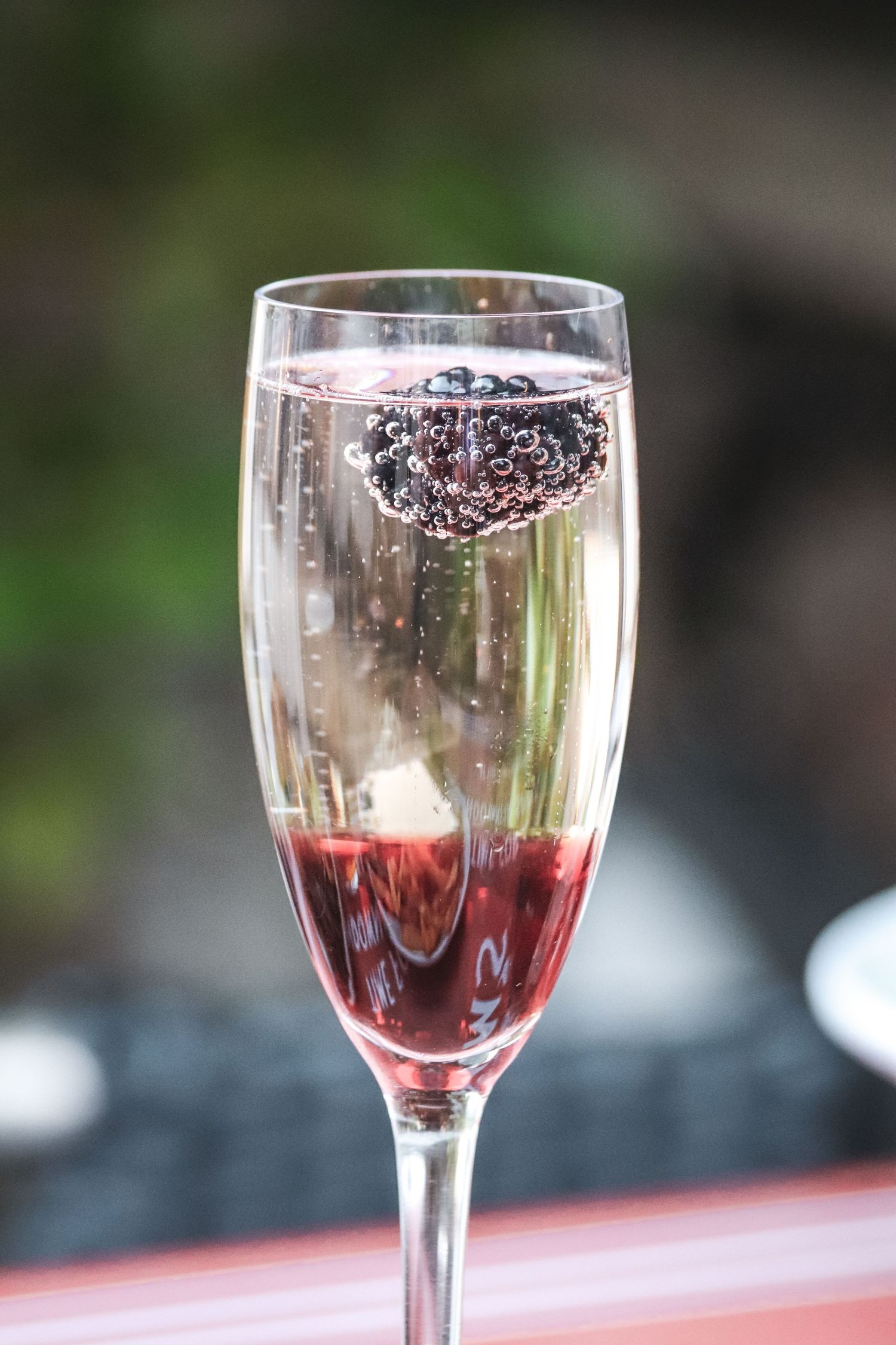 Close-up view of red wine being poured into a crystal glass against a blurred outdoor background.