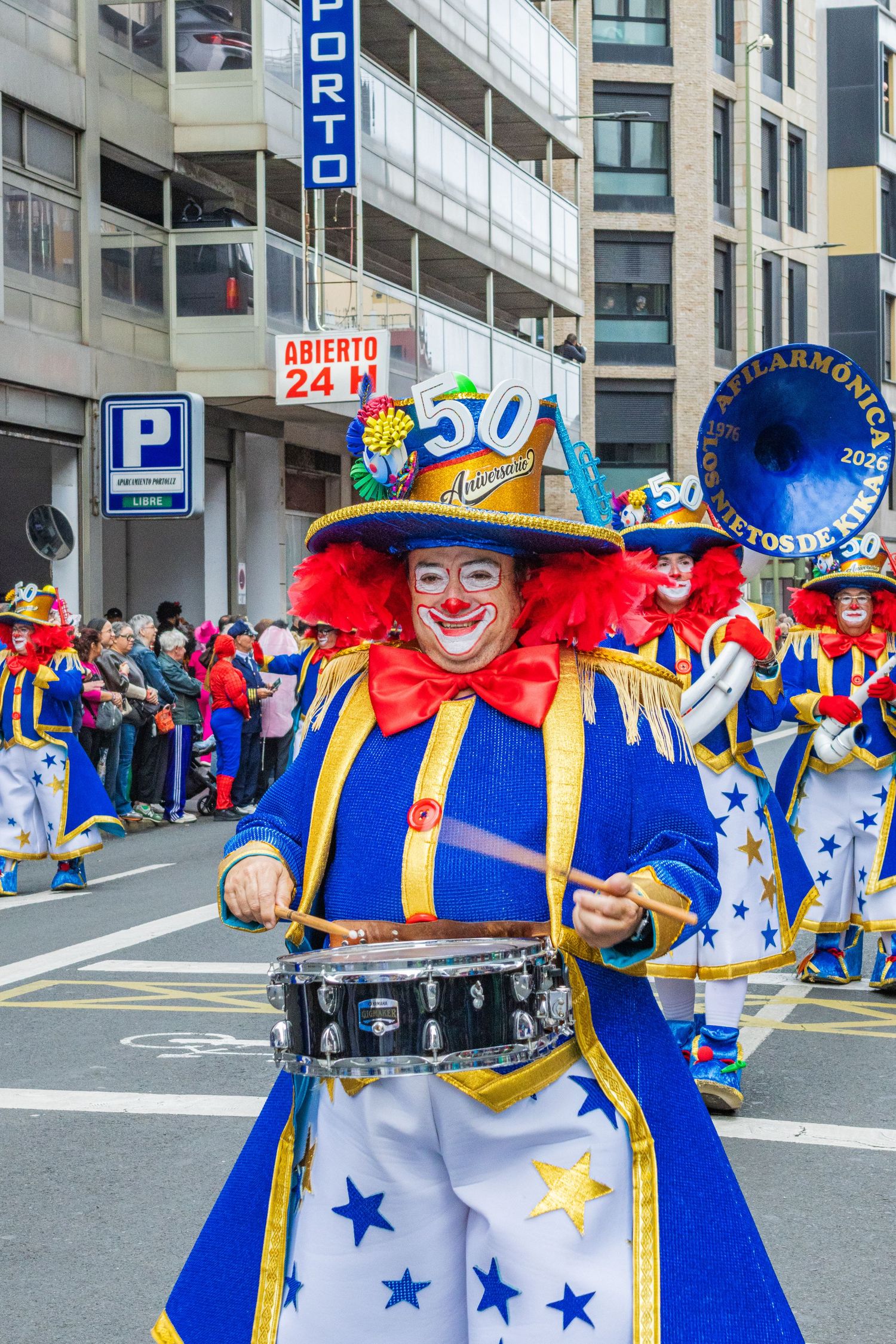 Colorful carnival performer in blue and white costume plays drum during street parade celebration.