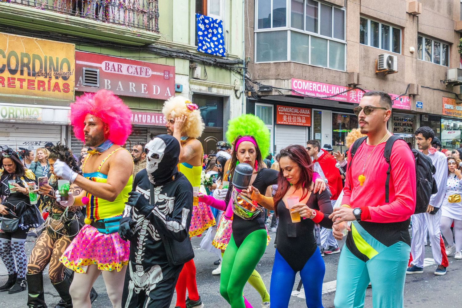 Colorful parade performers in vibrant costumes dancing and celebrating during a street festival in an urban setting.