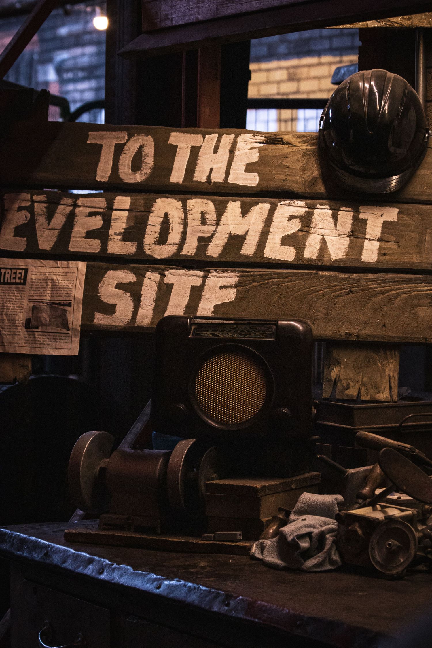 Rustic wooden signs with text 'TO THE SITE' illuminated in dark industrial setting with scattered equipment.