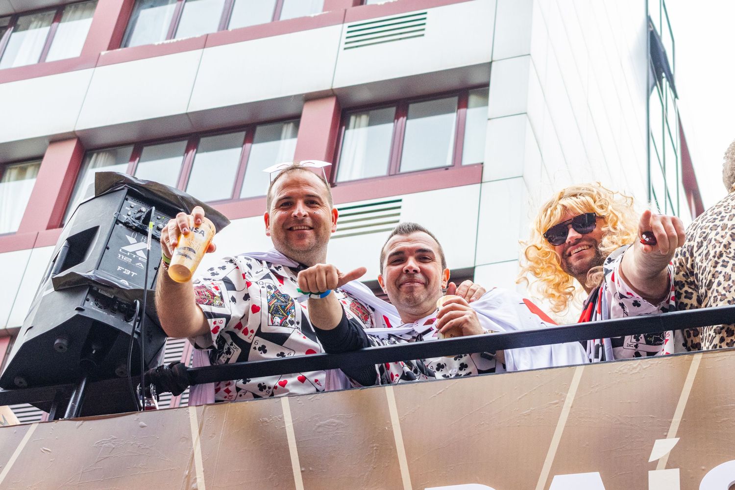 A large crowd of people waves and cheers from a balcony at a celebratory event.