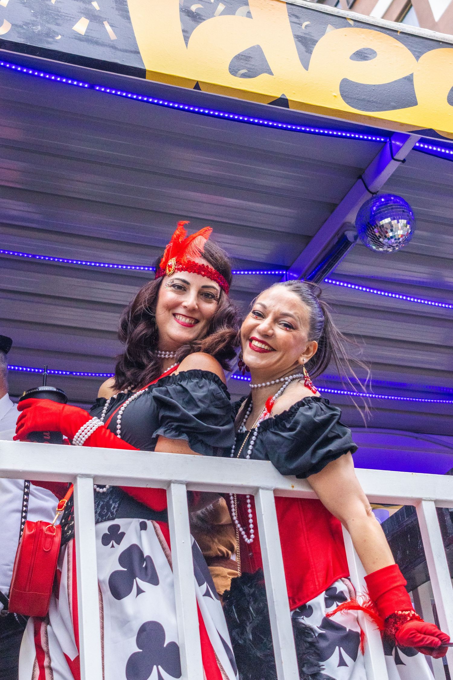 Carnival performers in red and black costumes wave from a parade float decorated with playing card symbols.