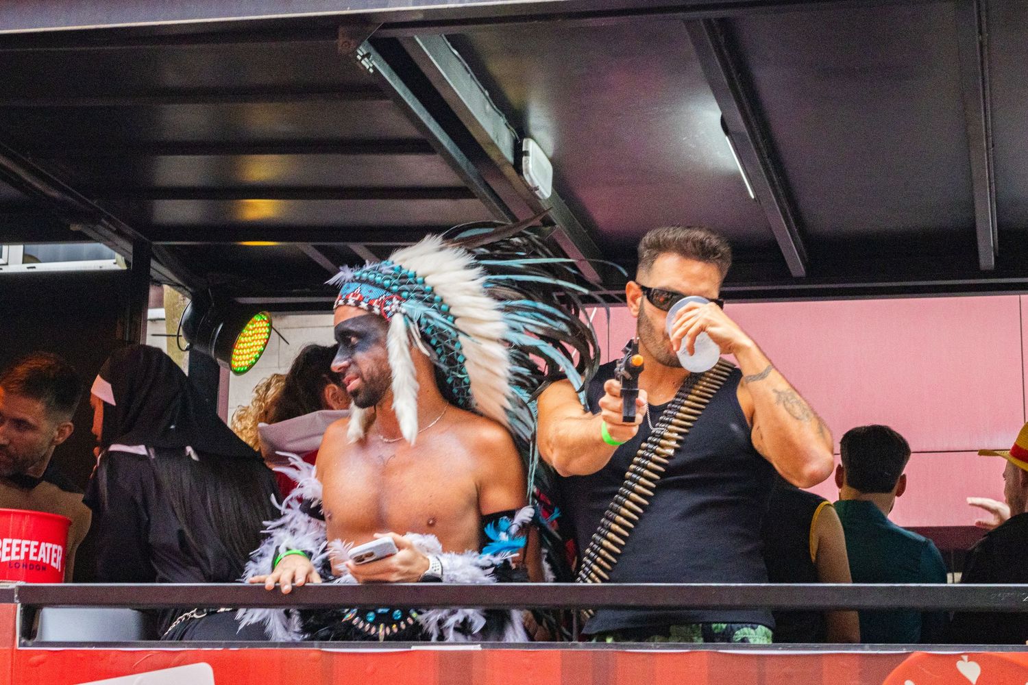 People perform at an event wearing a Native American headdress and drinking from bottles in a dark venue.