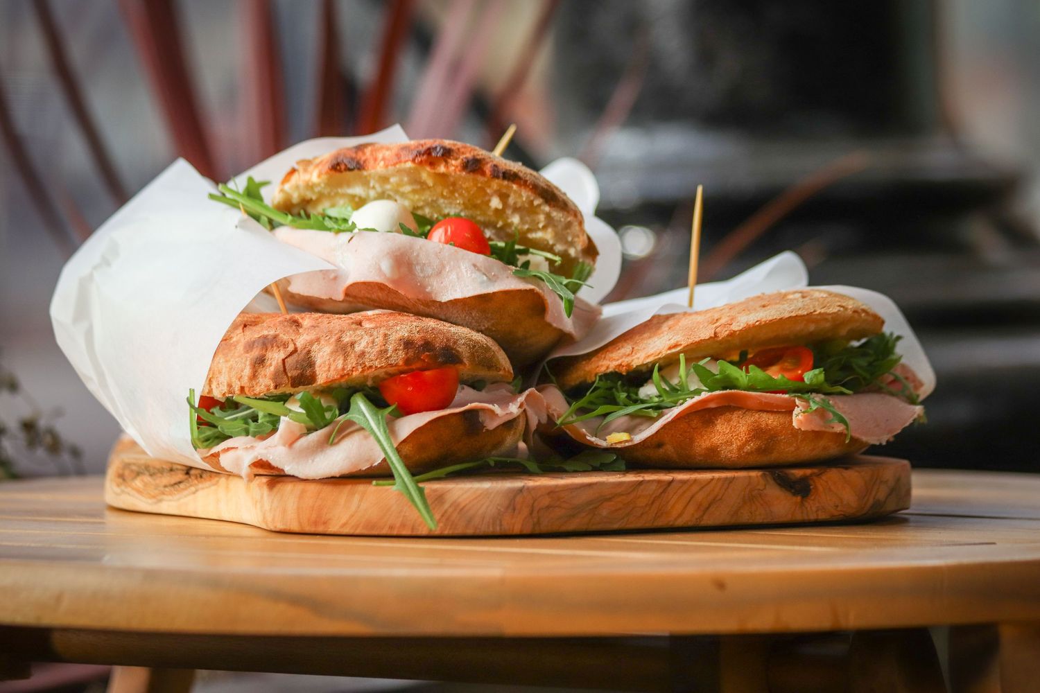 Fresh submarine sandwiches with cold cuts, vegetables and herbs arranged in a row on wooden cutting boards.