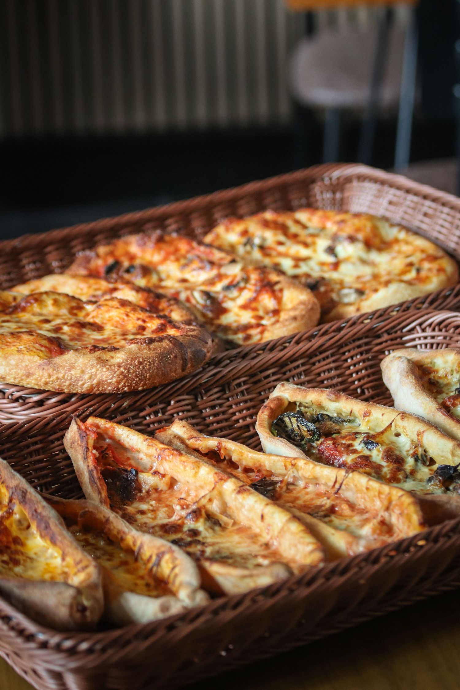 Freshly baked pizzas with melted cheese and toppings arranged on wooden serving boards in a dimly lit setting.