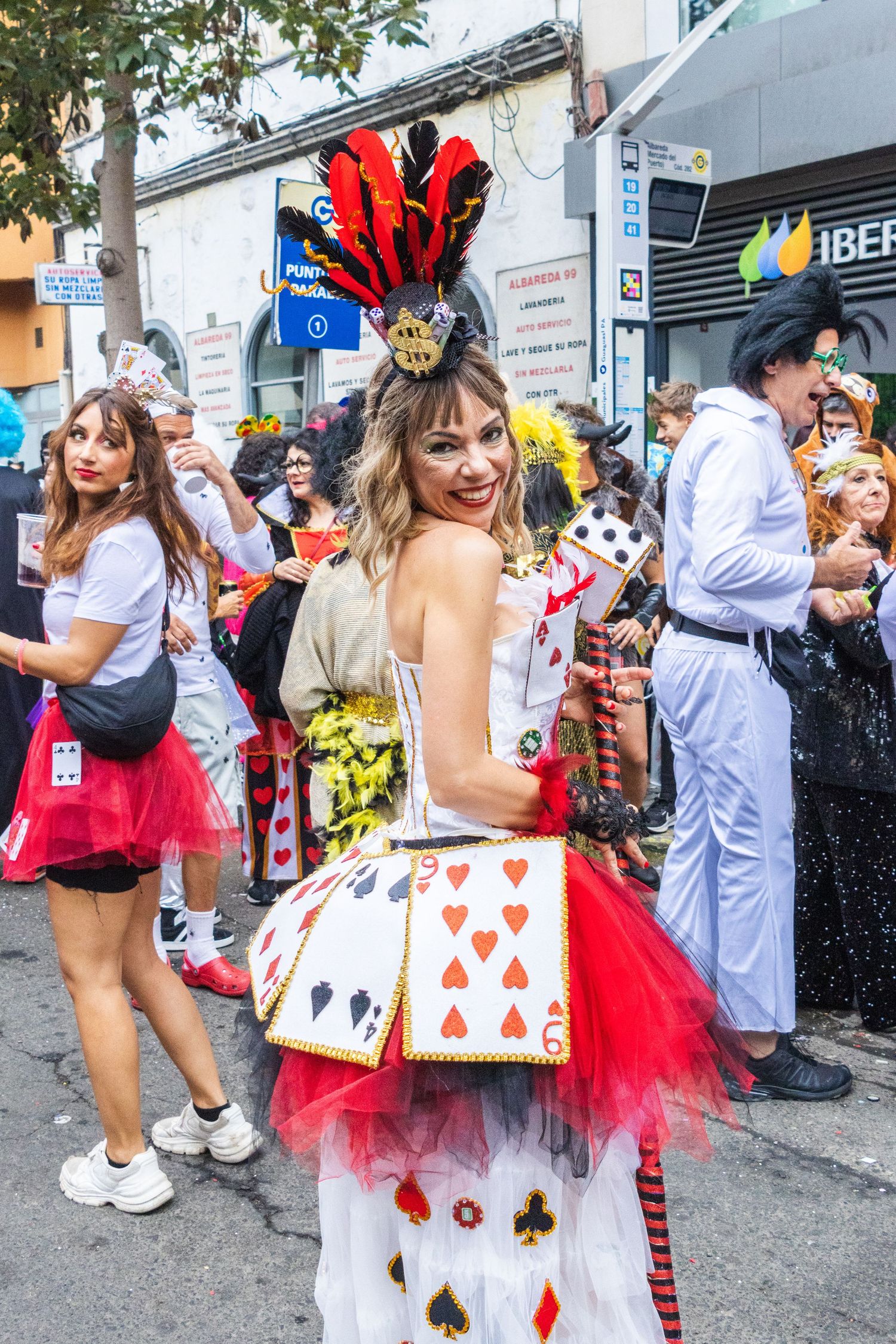 Carnival participants wearing festive playing card and queen of hearts themed costumes with red tutus at a street parade.