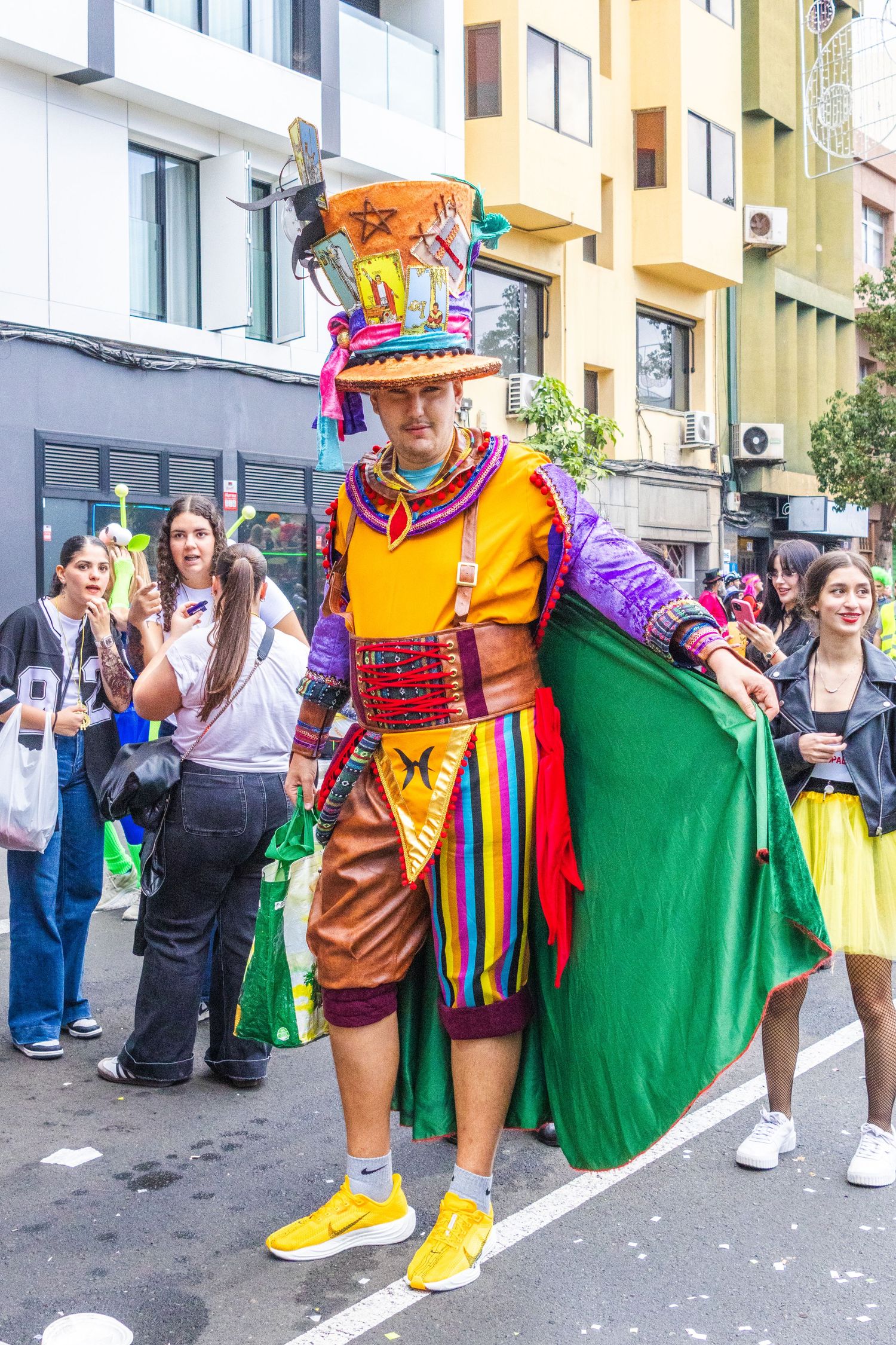 Colorfully dressed carnival performers in vibrant costumes with green capes entertain crowds at a street festival.