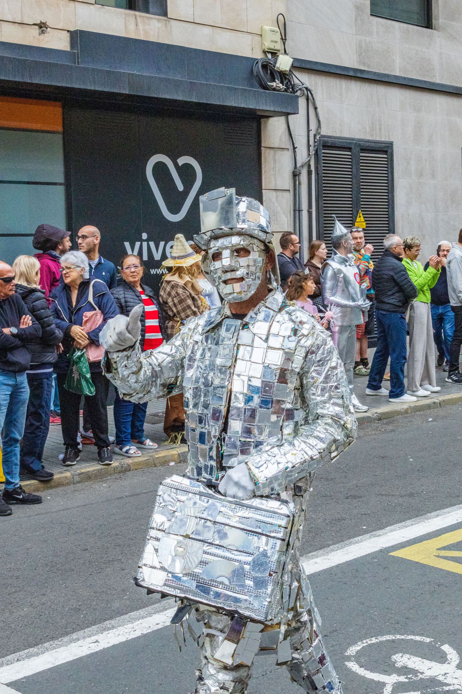 Street performers in silver metallic costumes entertain a crowd of onlookers outside a building.