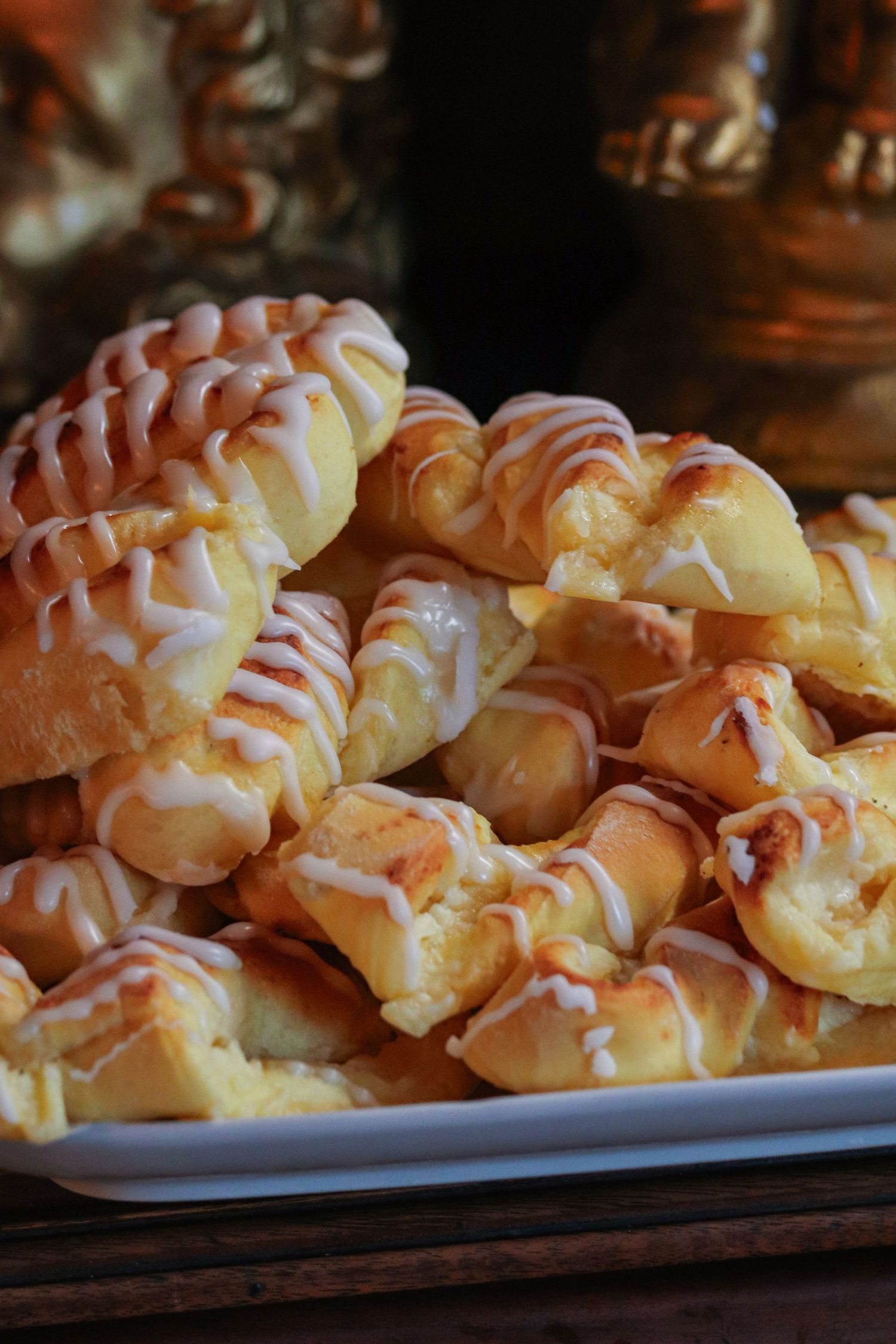 Freshly baked cream puffs drizzled with white icing arranged on a dark serving platter.