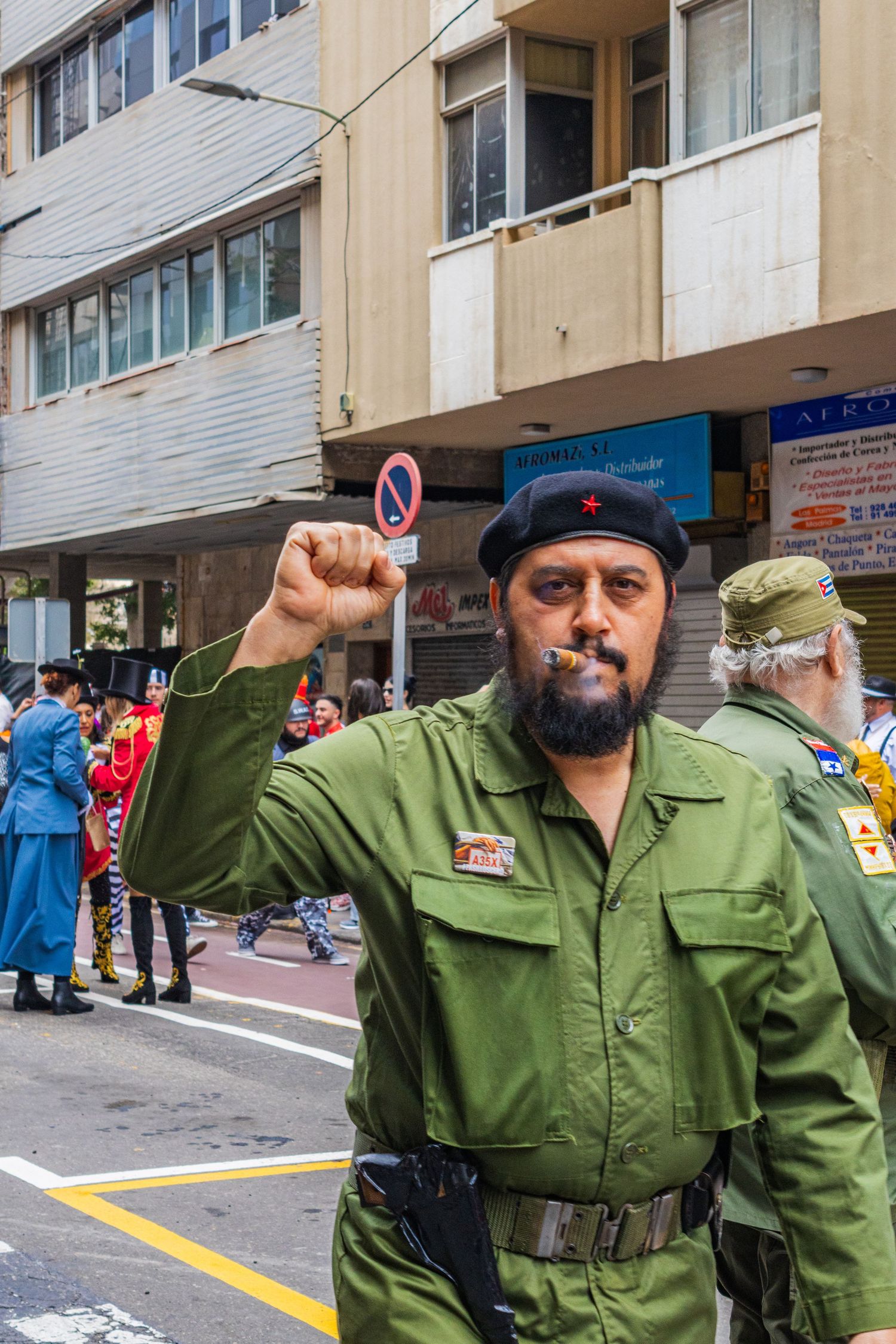 Person in green military-style uniform and beret raises fist in multiple similar poses on city street.