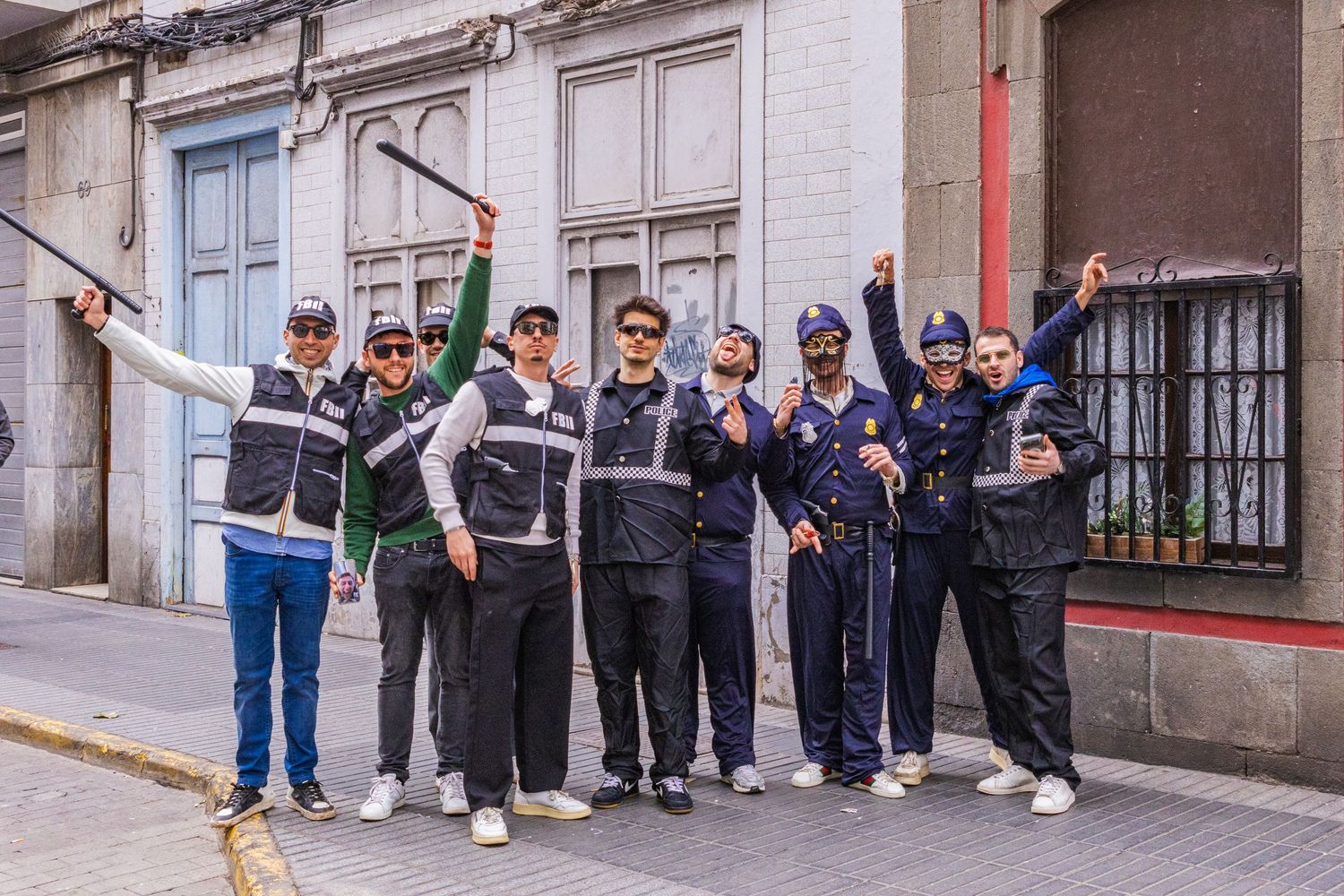 A group of people standing in a line against a white building wall waiting to enter.