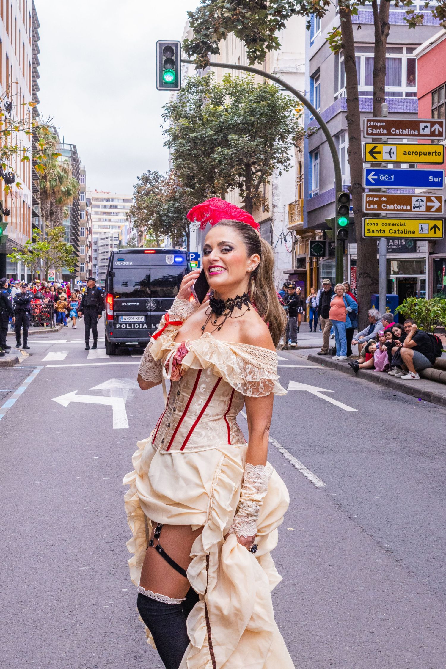 Woman in vintage-style costume with red headband and cream dress poses on city street during festival or parade.