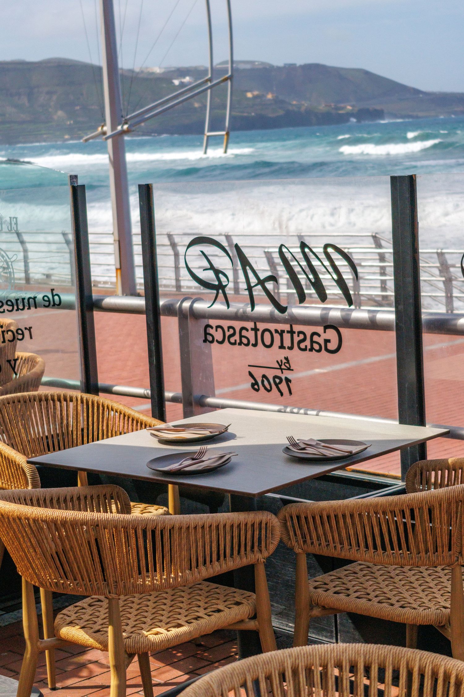 Seaside restaurant terrace with wicker chairs, dark tables, and ocean views at Mar Gastrotasca.
