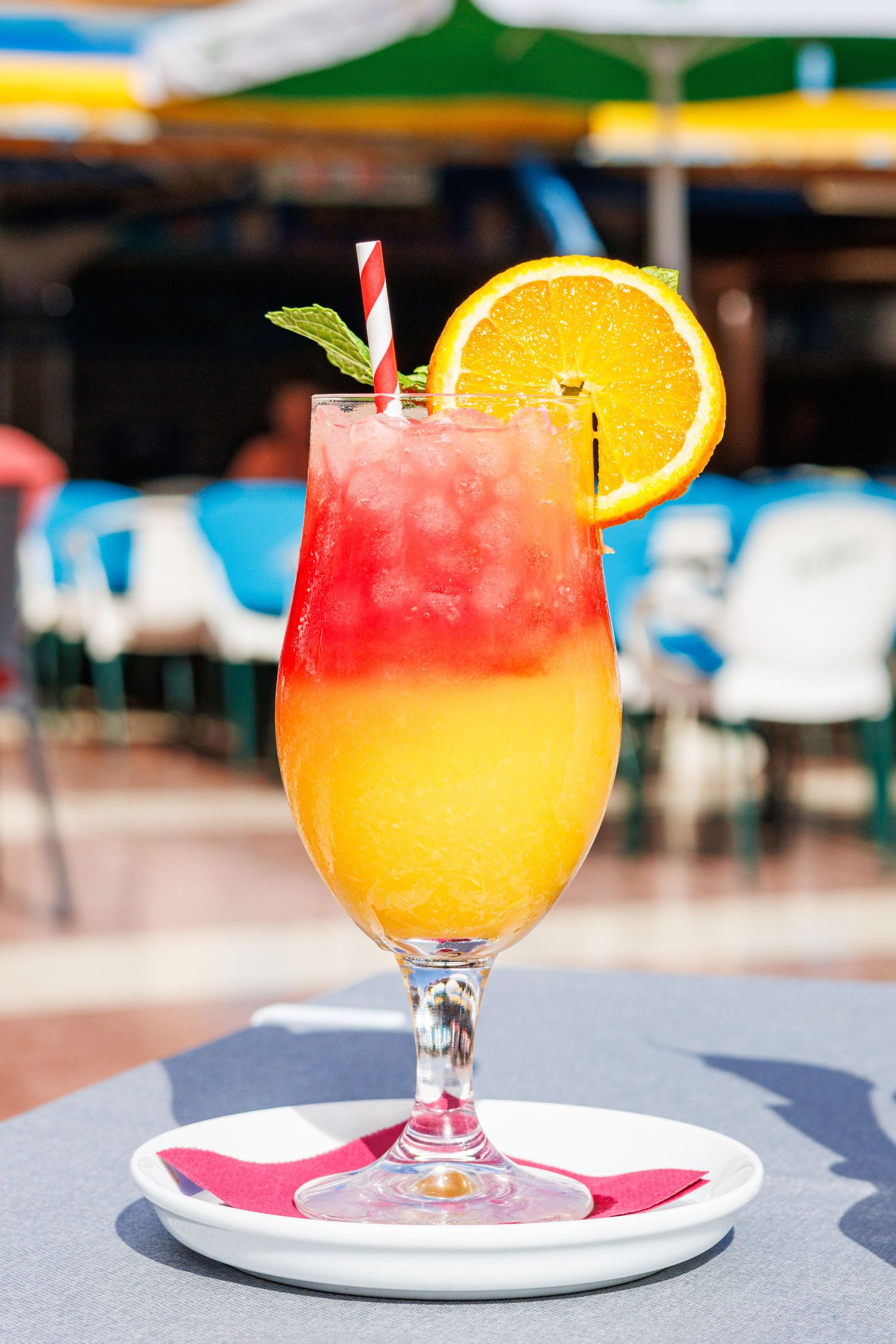 Tequila Sunrise cocktail with orange slice, mint, and straw on outdoor cafe table.
