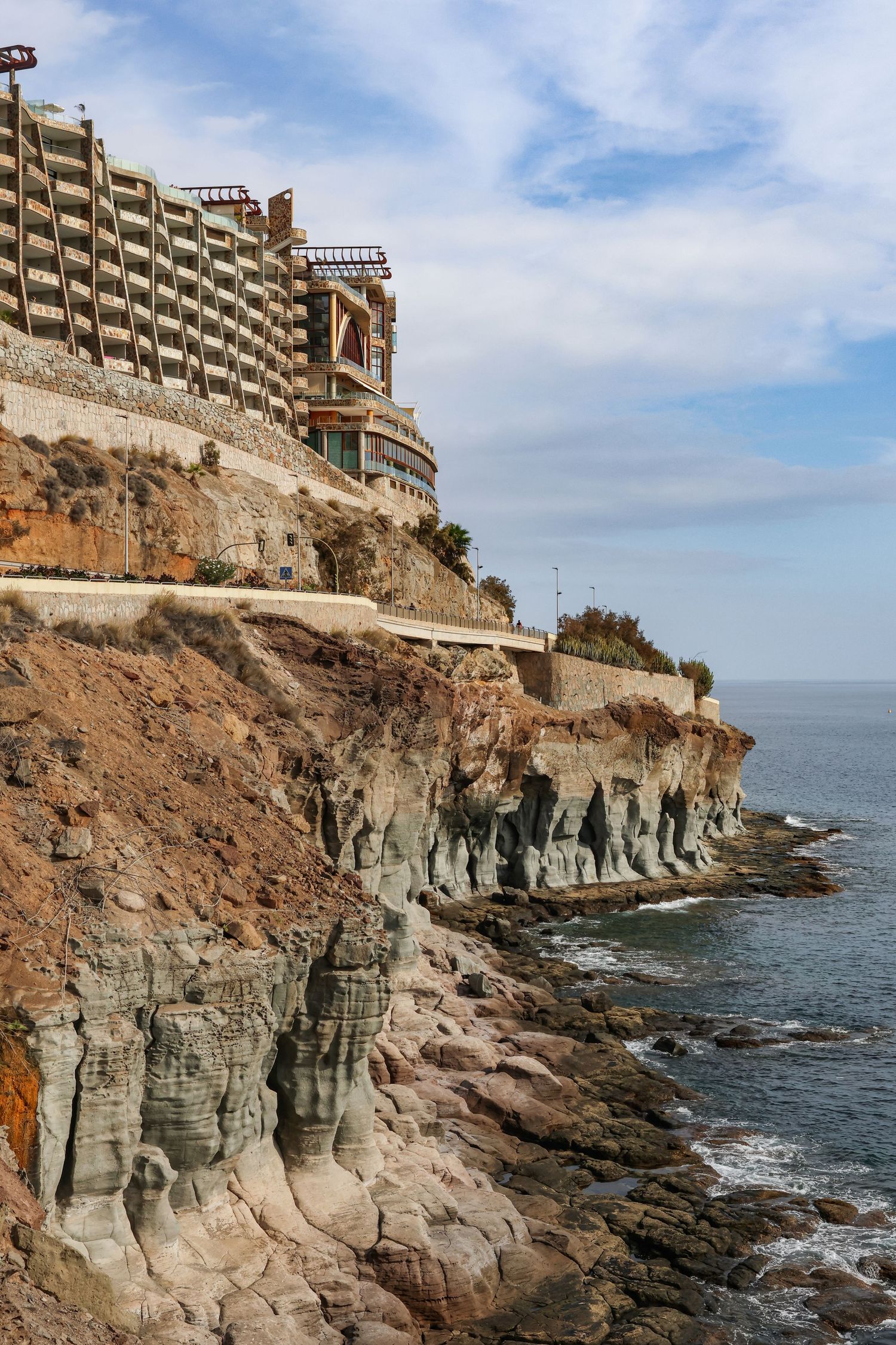 Coastal cliffs with modern hotel buildings perched on top overlooking the rocky Mediterranean shoreline.