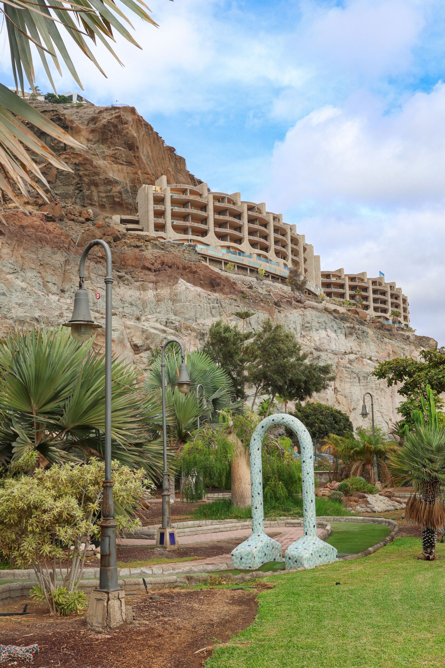 Modern terraced hotel built into rocky cliffs with tropical landscaping and decorative arch in Gran Canaria, Spain.