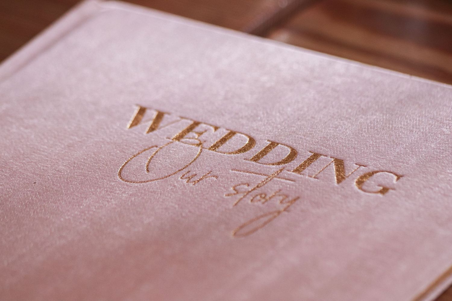 Wedding photo albums with gold lettering and pink blush covers arranged in a row on a light surface.