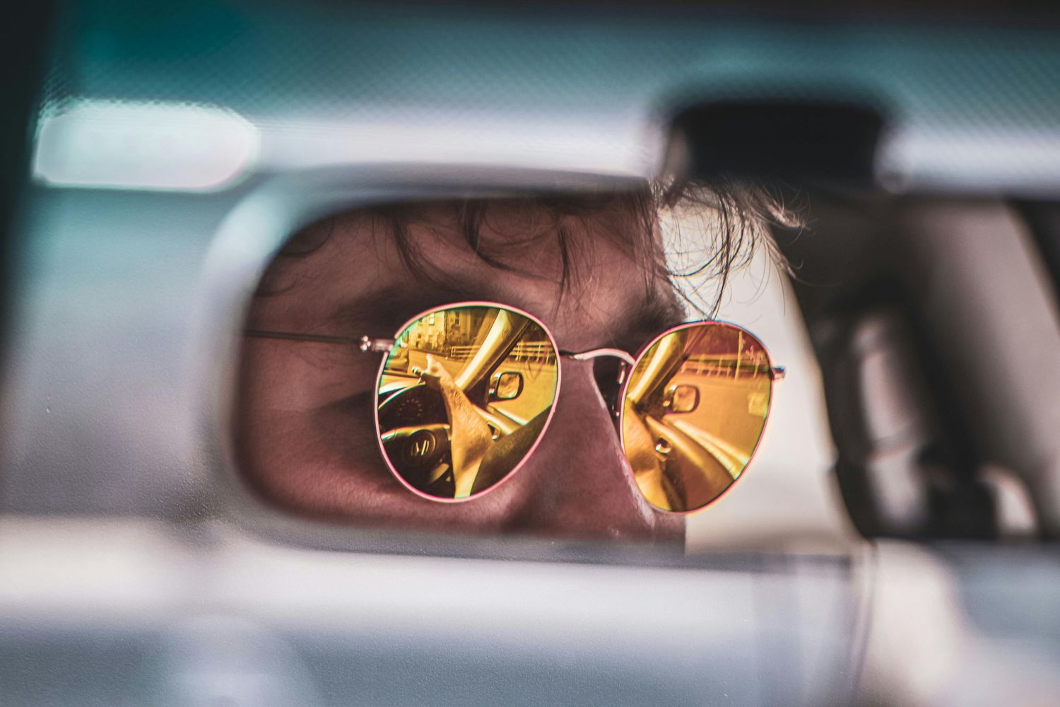 Reflection of sunlight in rearview mirror of car creating golden lens flare effect.