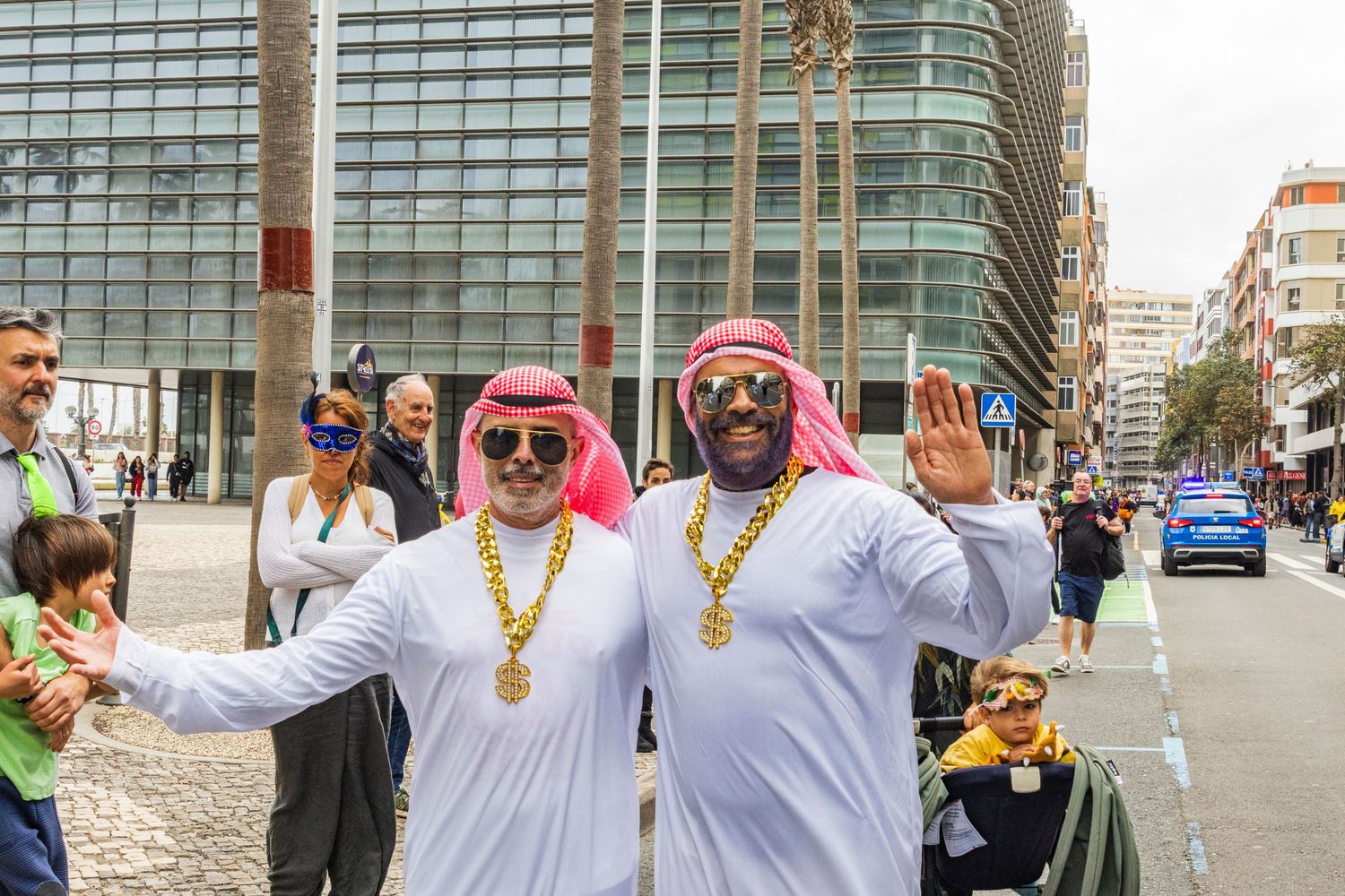 Group of people in traditional white robes and colorful accessories celebrate during a festival in an urban setting.