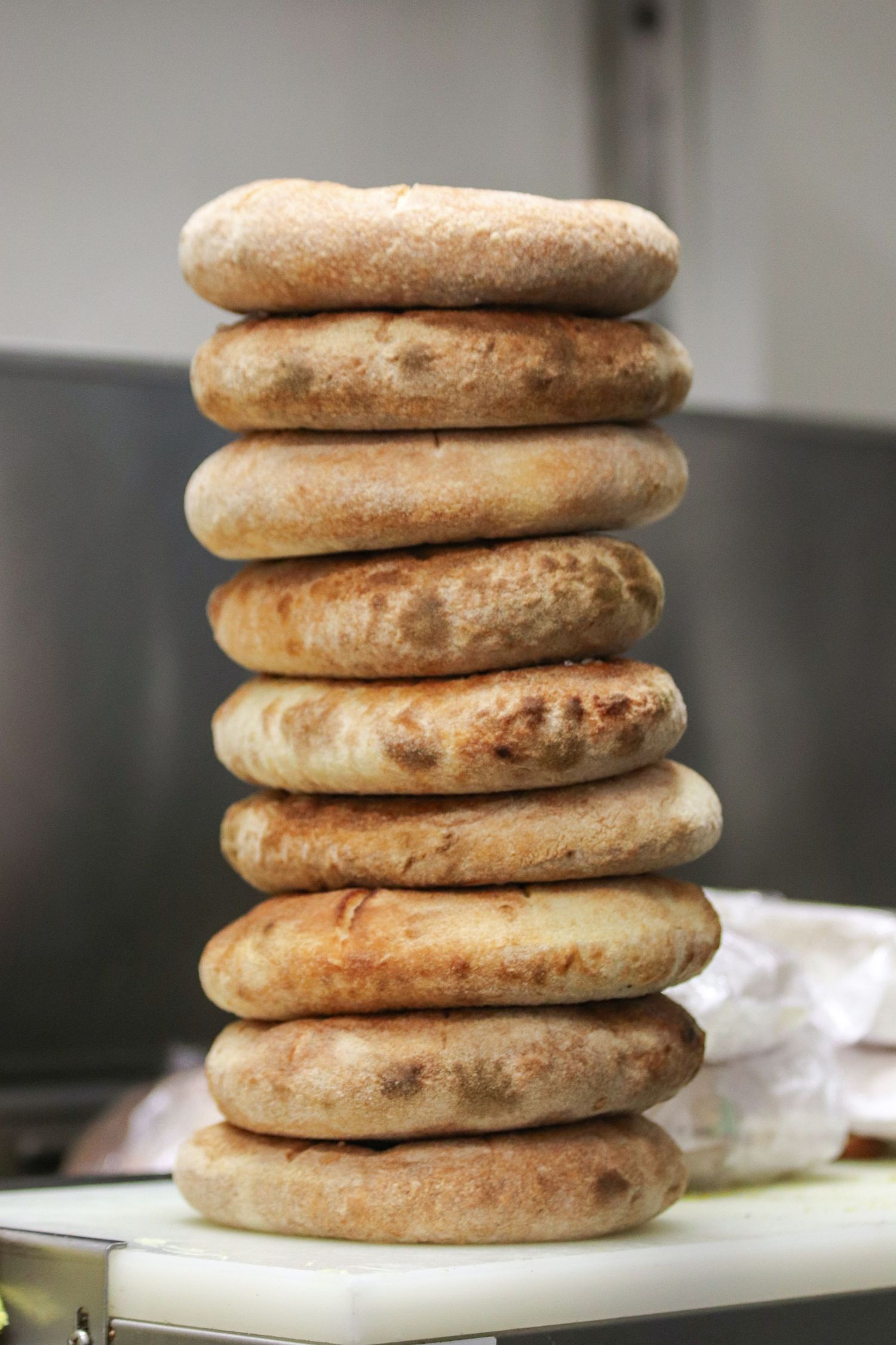 A tall stack of freshly baked English muffins with golden brown crusts piled on a white surface.