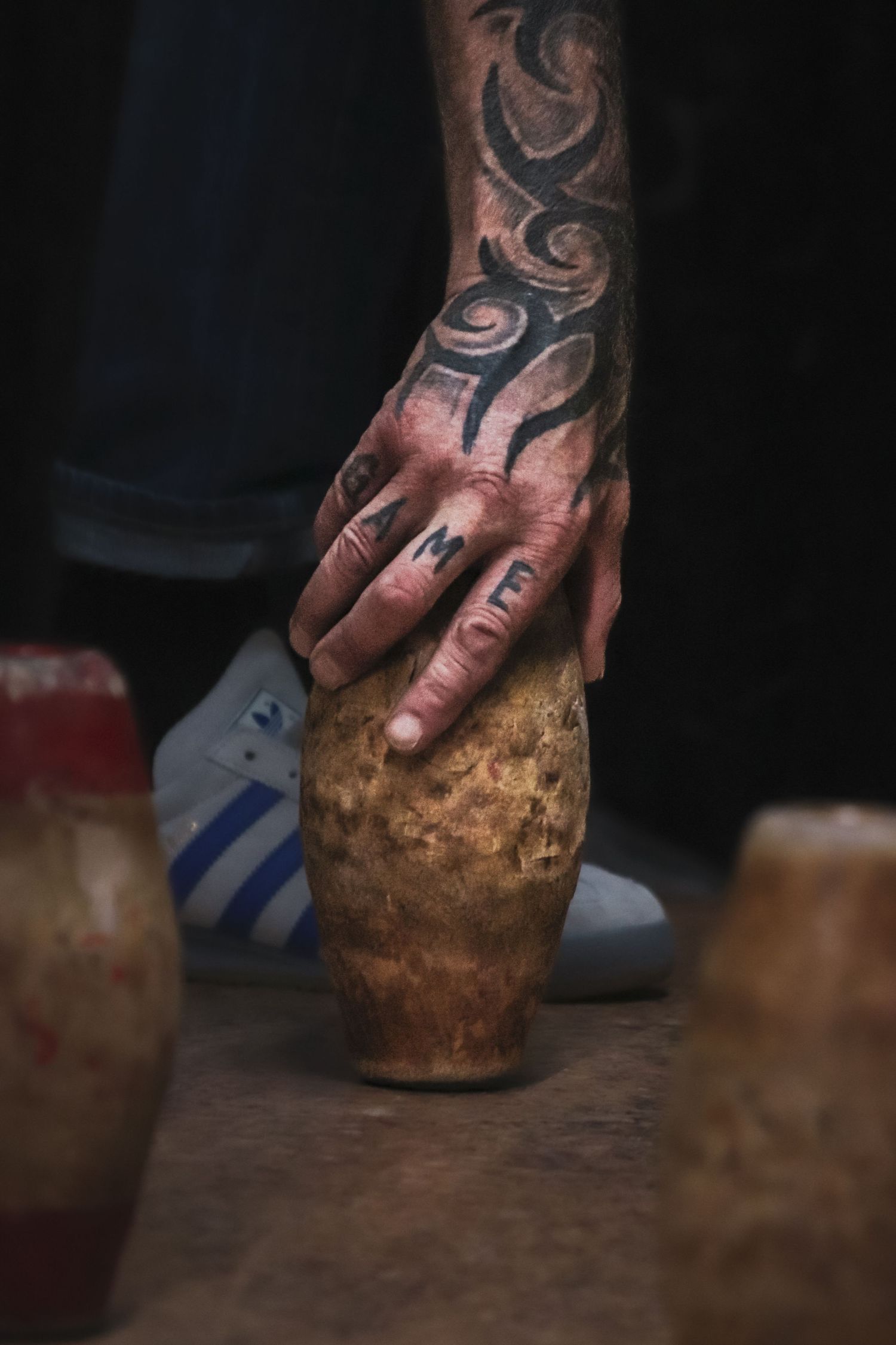 A tattooed hand holds a raw sweet potato on a rustic wooden surface in dramatic lighting.