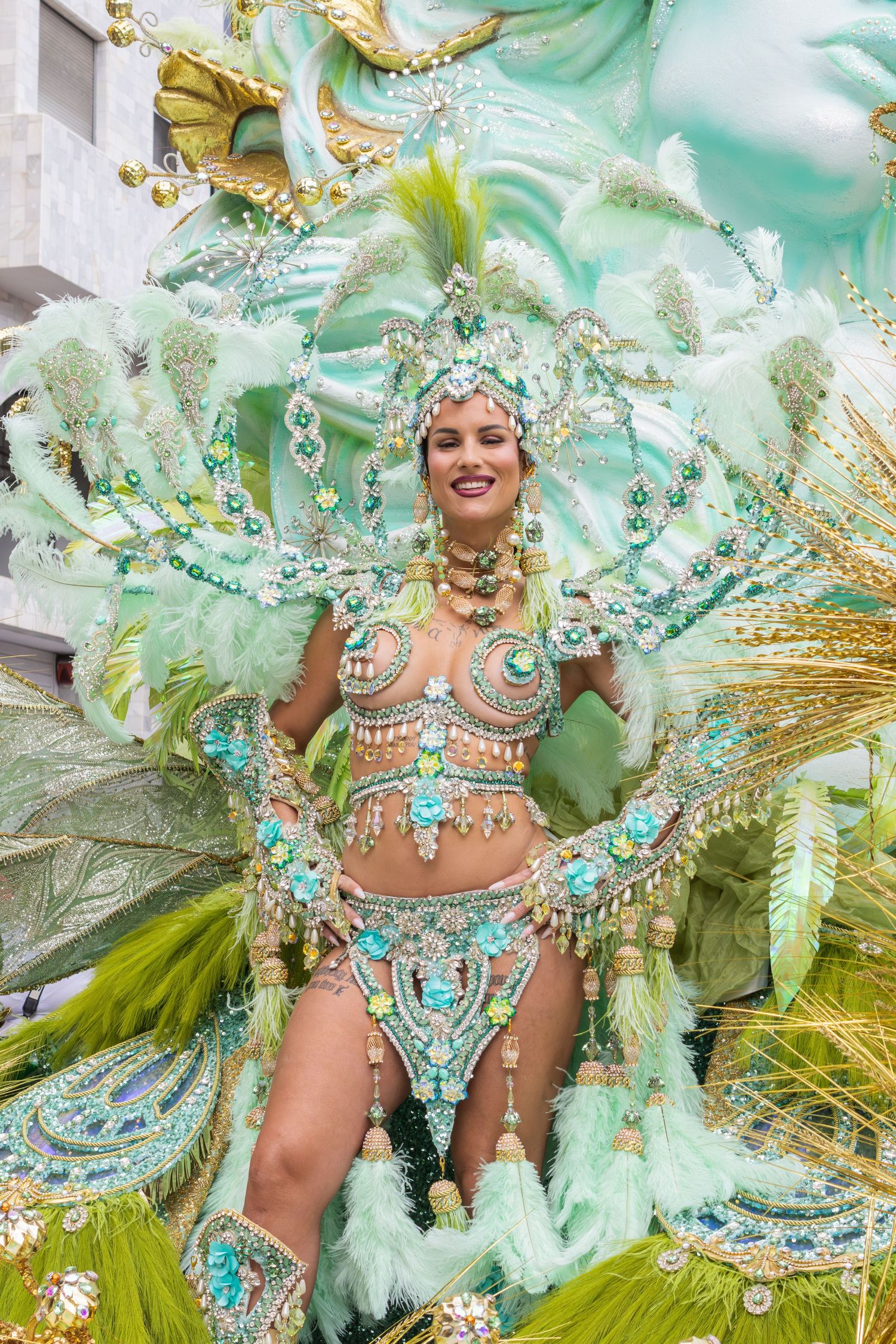 Carnival dancer in elaborate mint green and gold feathered costume with jeweled details performs at festival celebration.
