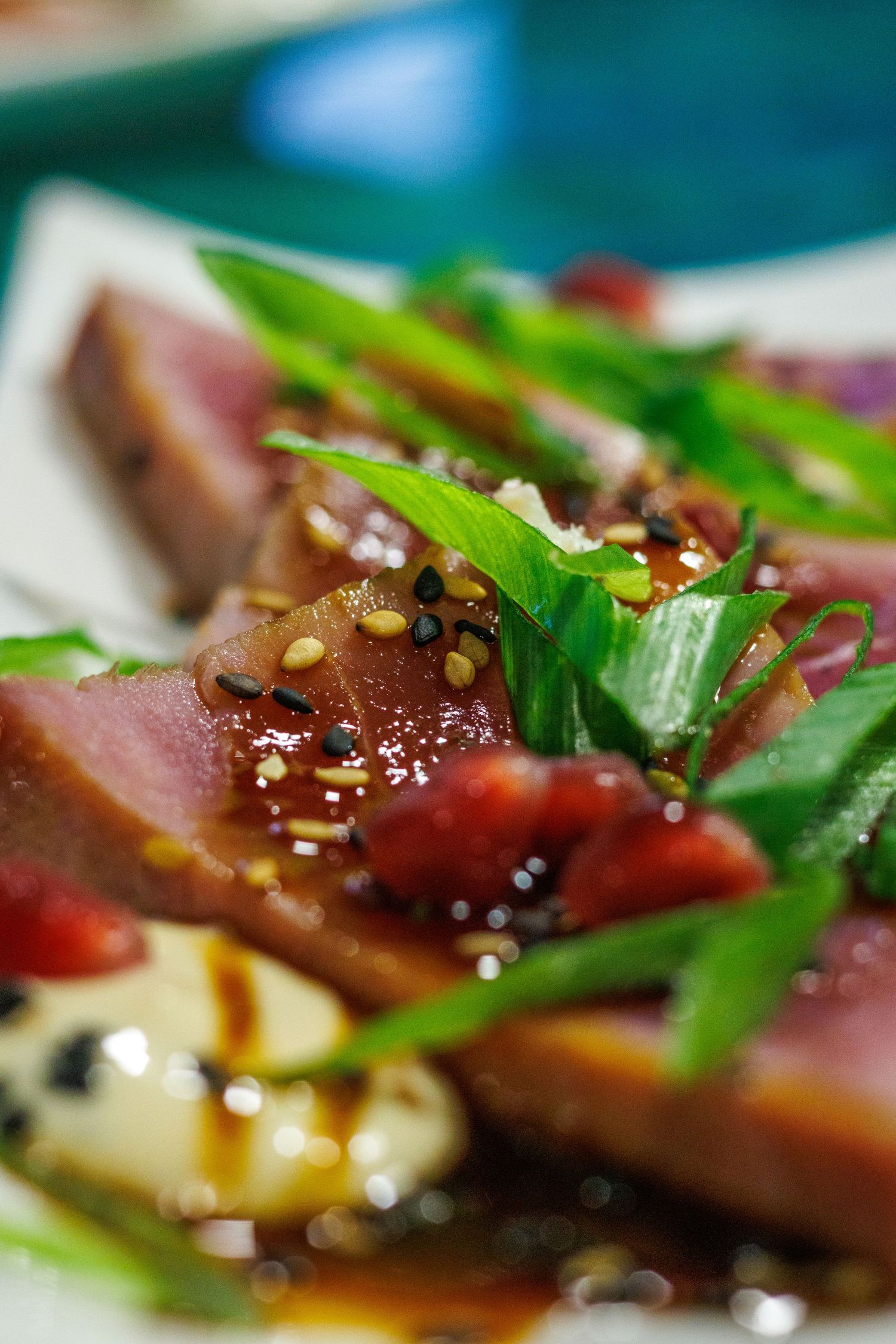 Seared tuna slices topped with fresh herbs, sesame seeds, and drizzled with savory sauce on a white plate.