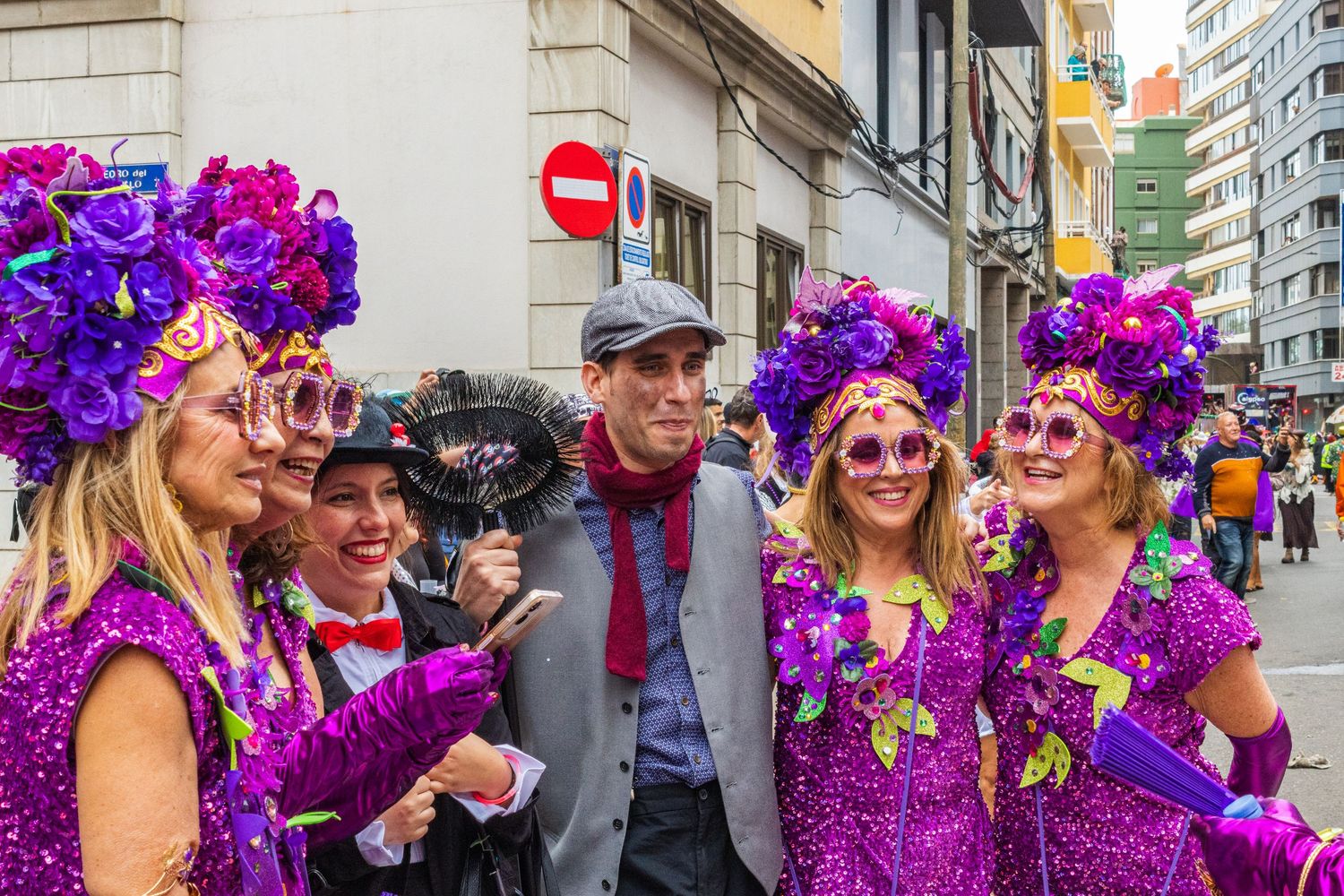 Carnival performers wearing vibrant purple sequined costumes and floral headdresses celebrate during a street festival.