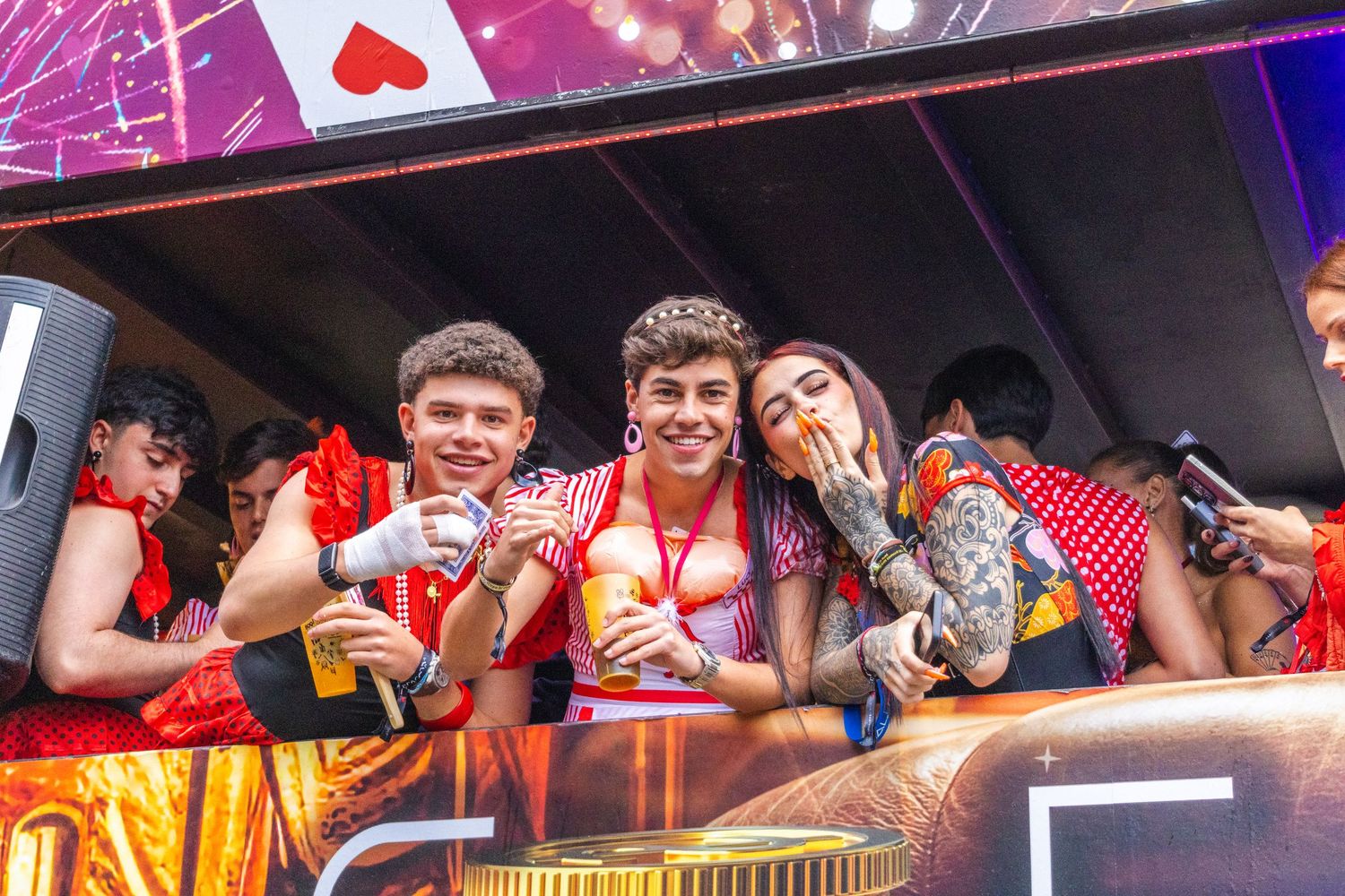 A crowd of people enjoying drinks and entertainment at a lively bar with colorful pink and purple lighting.